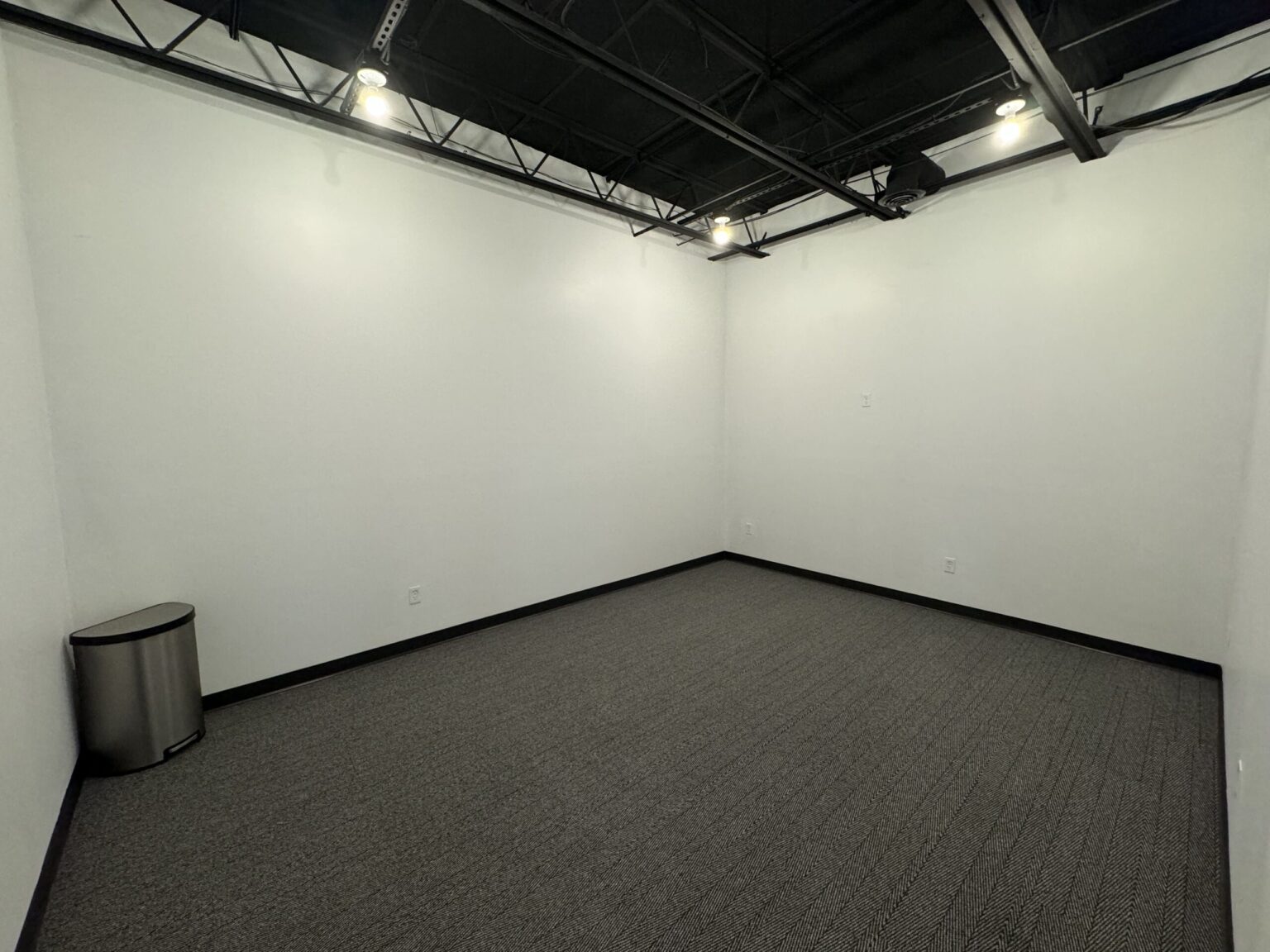 Empty carpet-tiled room in a Saline commercial build-out with white walls and an open ceiling painted black