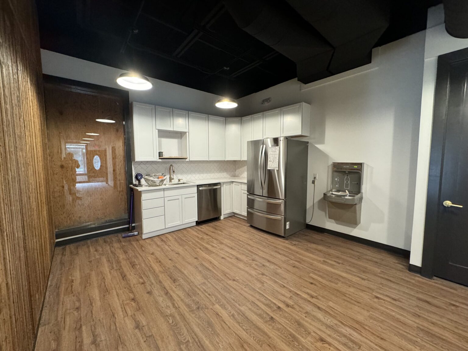 Office kitchen in a Saline commercial build-out with white shaker cabinets, a stainless refrigerator, a bottle-filling drinking fountain and a wood slat wall