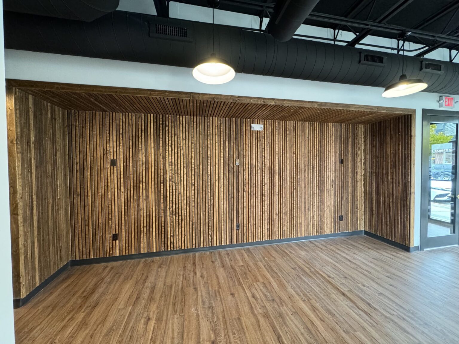 Wide view of a vertical wood slat feature wall in a Saline office, framed by white walls under an open black ceiling with pendant lights