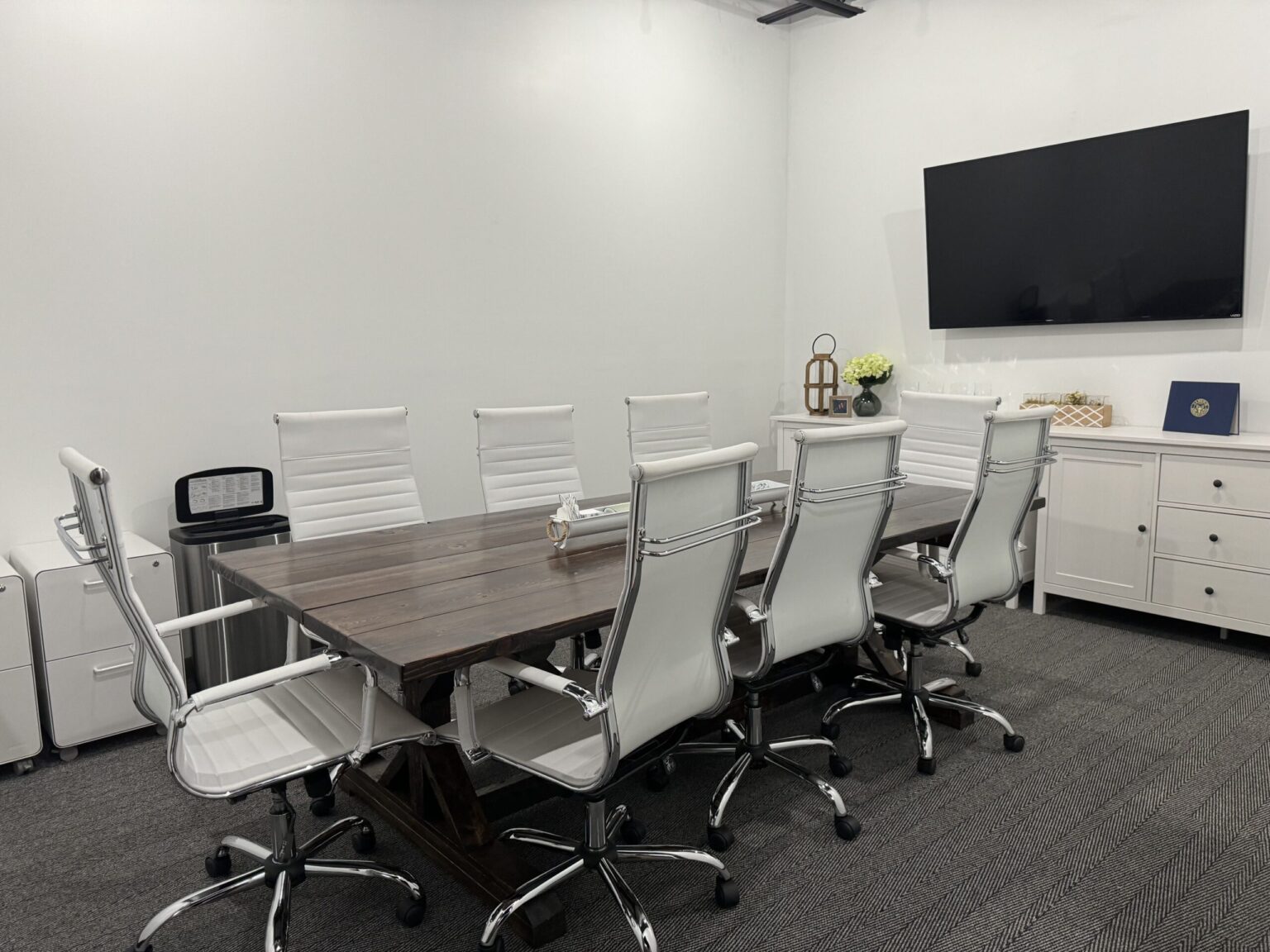 Finished conference room in a Saline office with a long table, white mesh chairs, a wall-mounted screen, white cabinets and gray carpet tile
