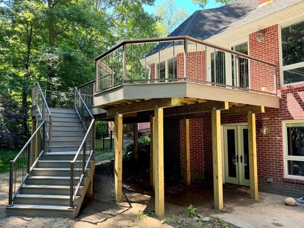 Raised deck on tall wood posts with a long stair, shown during construction beside a brick home
