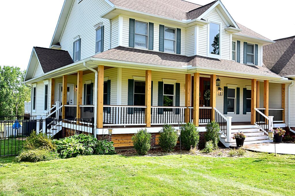 White farmhouse with a wraparound covered porch, new columns and railings, photographed from the corner