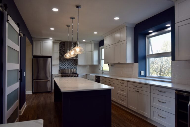 Saline kitchen with a navy island under glass pendants, white cabinets and a navy accent wall