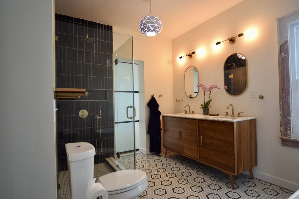 Bathroom with a dark vertical tile shower, wood vanity, two round mirrors and a patterned tile floor