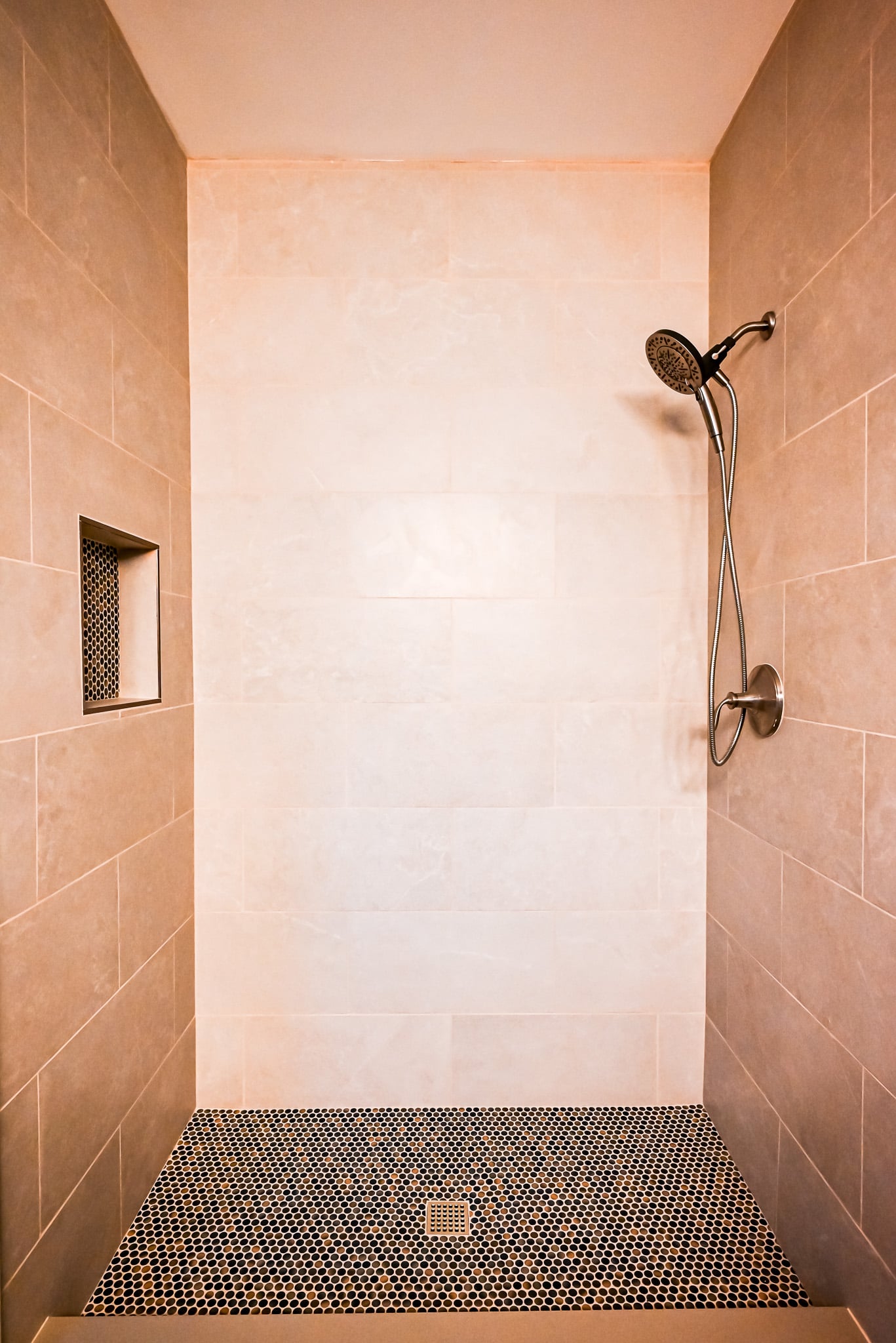 Walk-in shower with cream porcelain wall tile, dark penny round mosaic floor, recessed niche, and brushed nickel showerhead