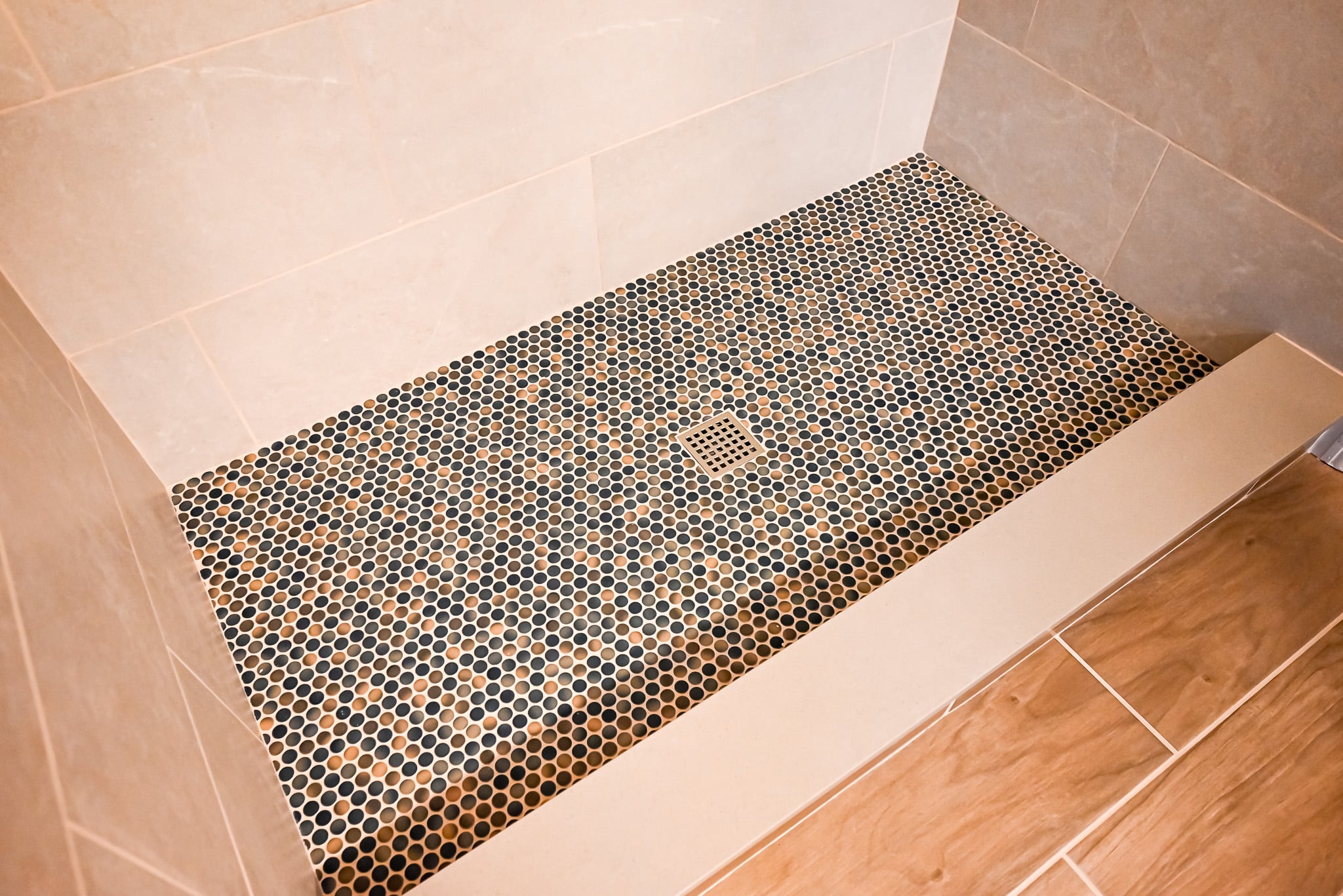 Overhead view of penny round mosaic shower floor with square center drain and cream tile curb