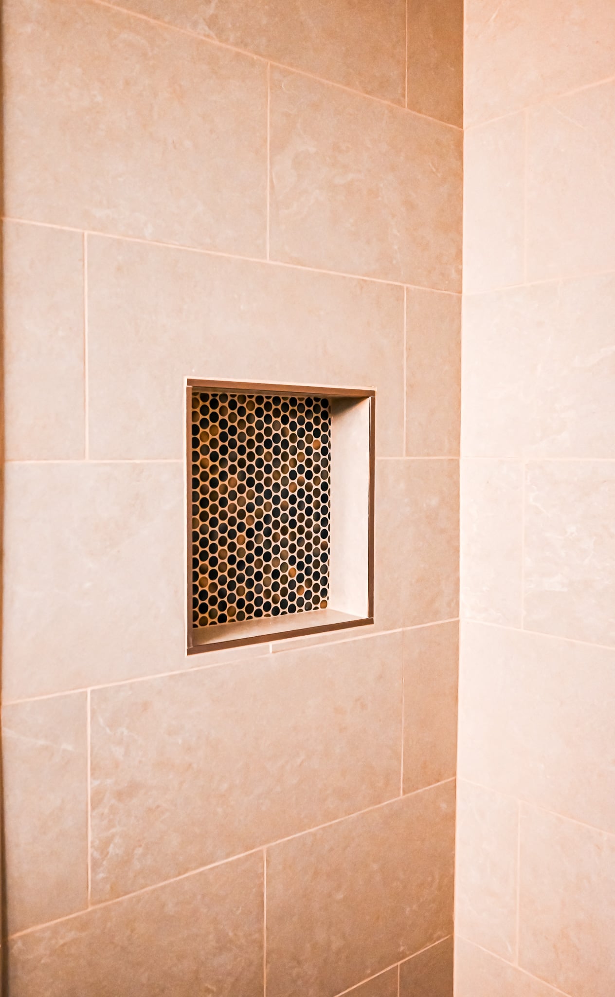 Close-up of recessed shower niche lined with penny round mosaic tile in black, bronze, and copper tones
