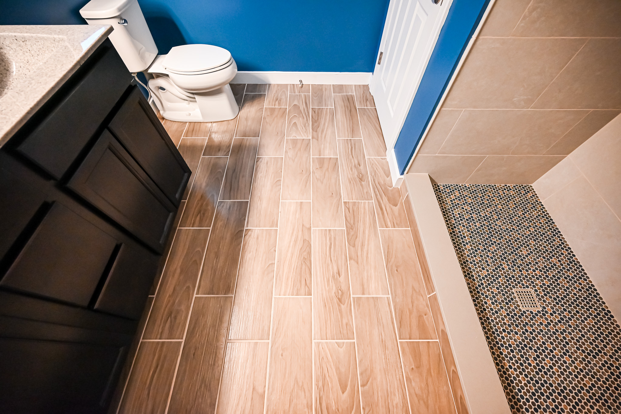 Overhead view of wood-look porcelain floor tile transitioning to penny round mosaic at the shower entry