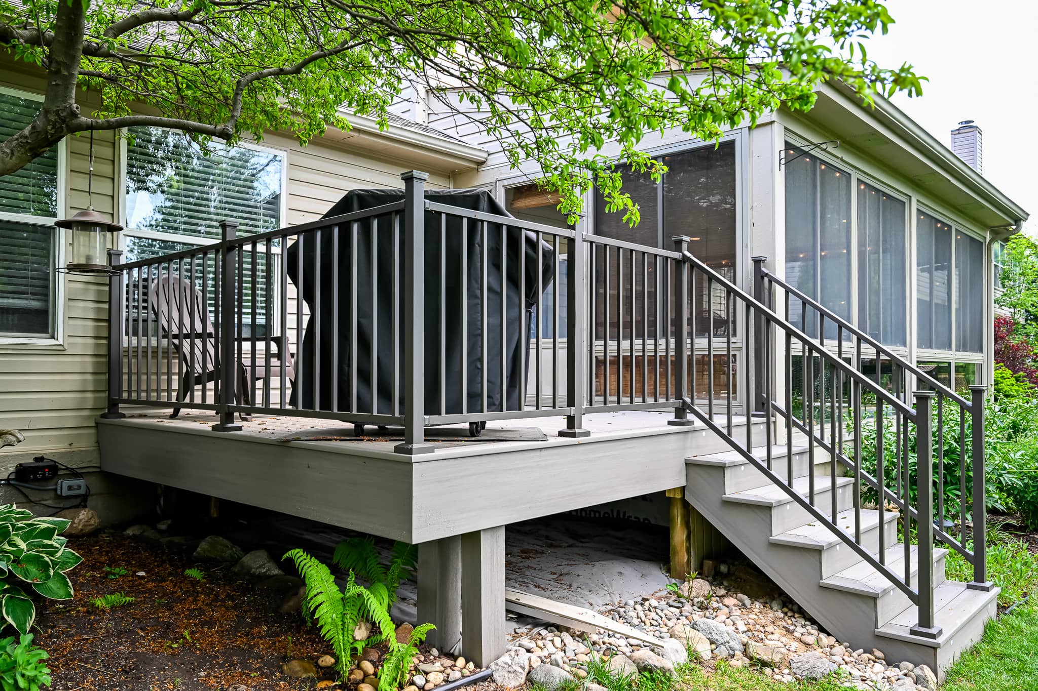 Composite deck with gray decking boards and dark metal-look railing, holding a covered grill, beside the screened porch on a Ypsilanti home