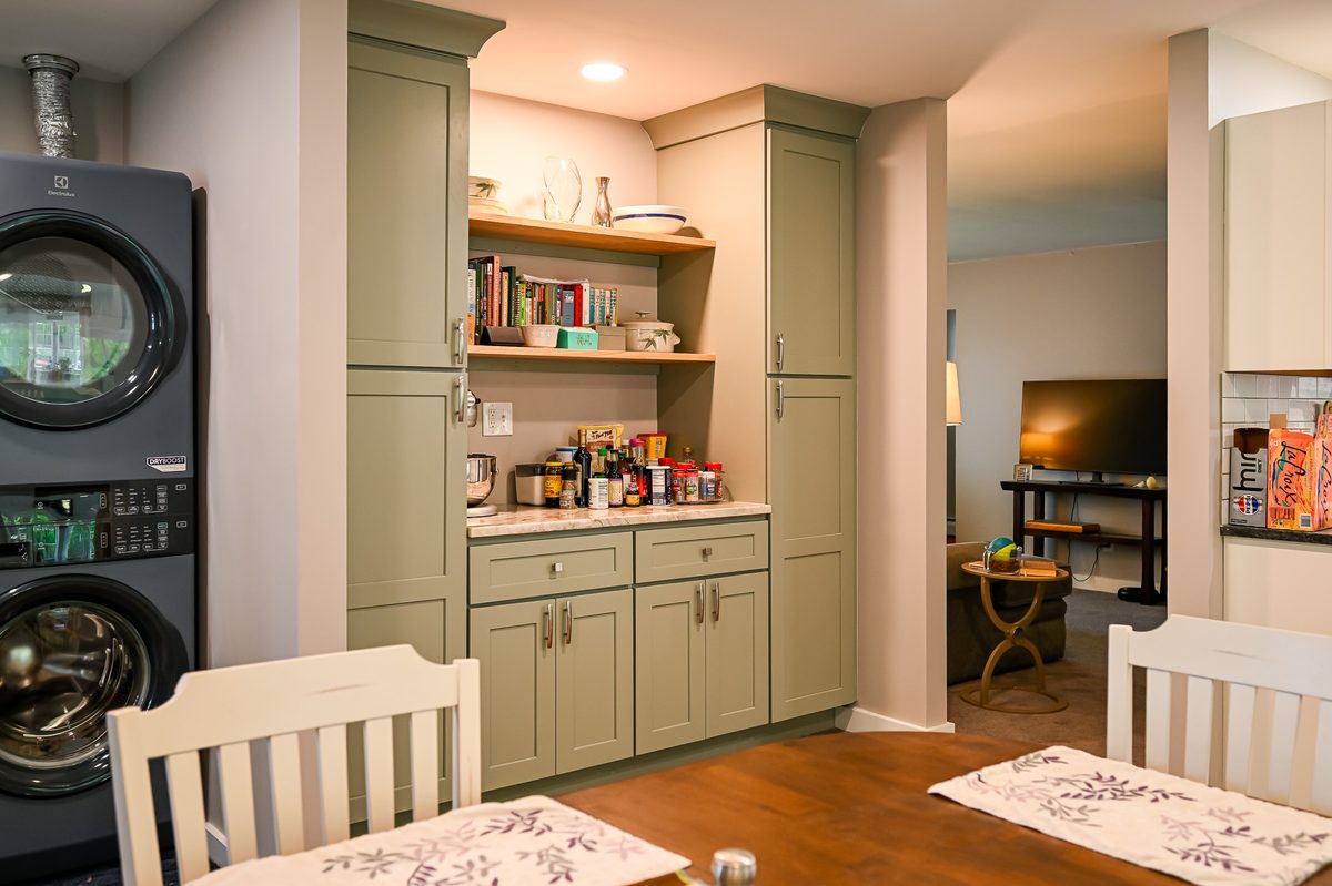 View from the dining table looking toward the pantry built-in and laundry area, showing how the sage green cabinetry connects the dining space, pantry, and laundry room into one cohesive design