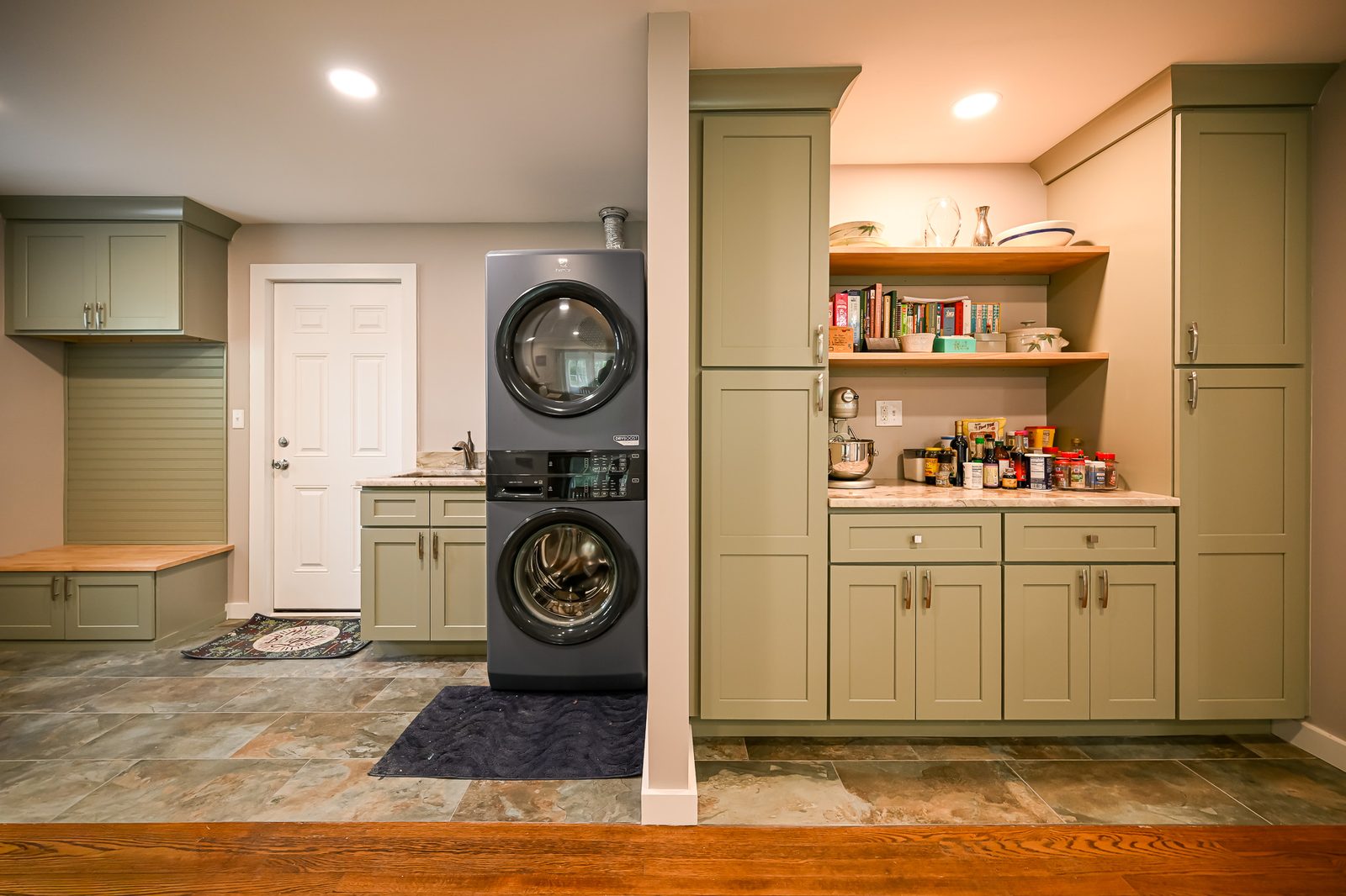 Wide view of the new laundry area with stacked Electrolux washer and dryer, sage green shaker cabinets, a utility sink with marble countertop, and the built-in pantry visible to the right