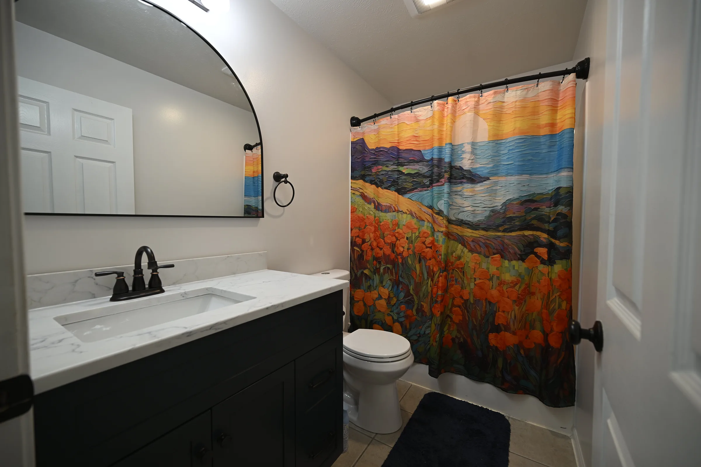 Renovated bathroom with dark vanity, quartz countertop, arched black-frame mirror, and oil-rubbed bronze faucet