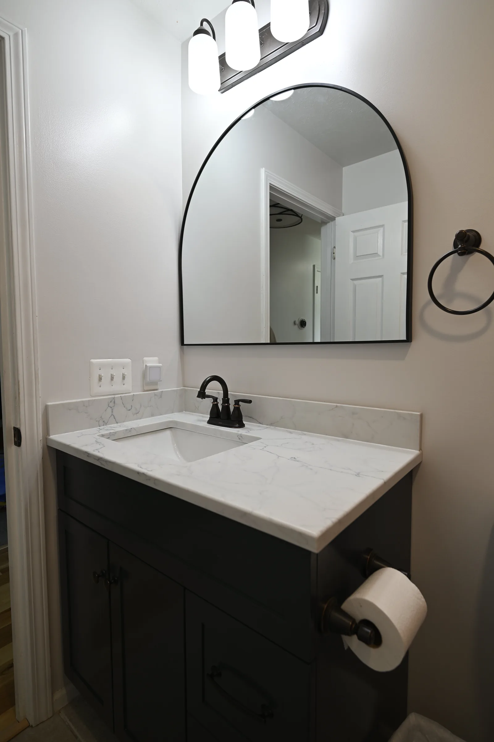 Bathroom vanity with black-framed arched mirror, quartz top, and oil-rubbed bronze fixtures