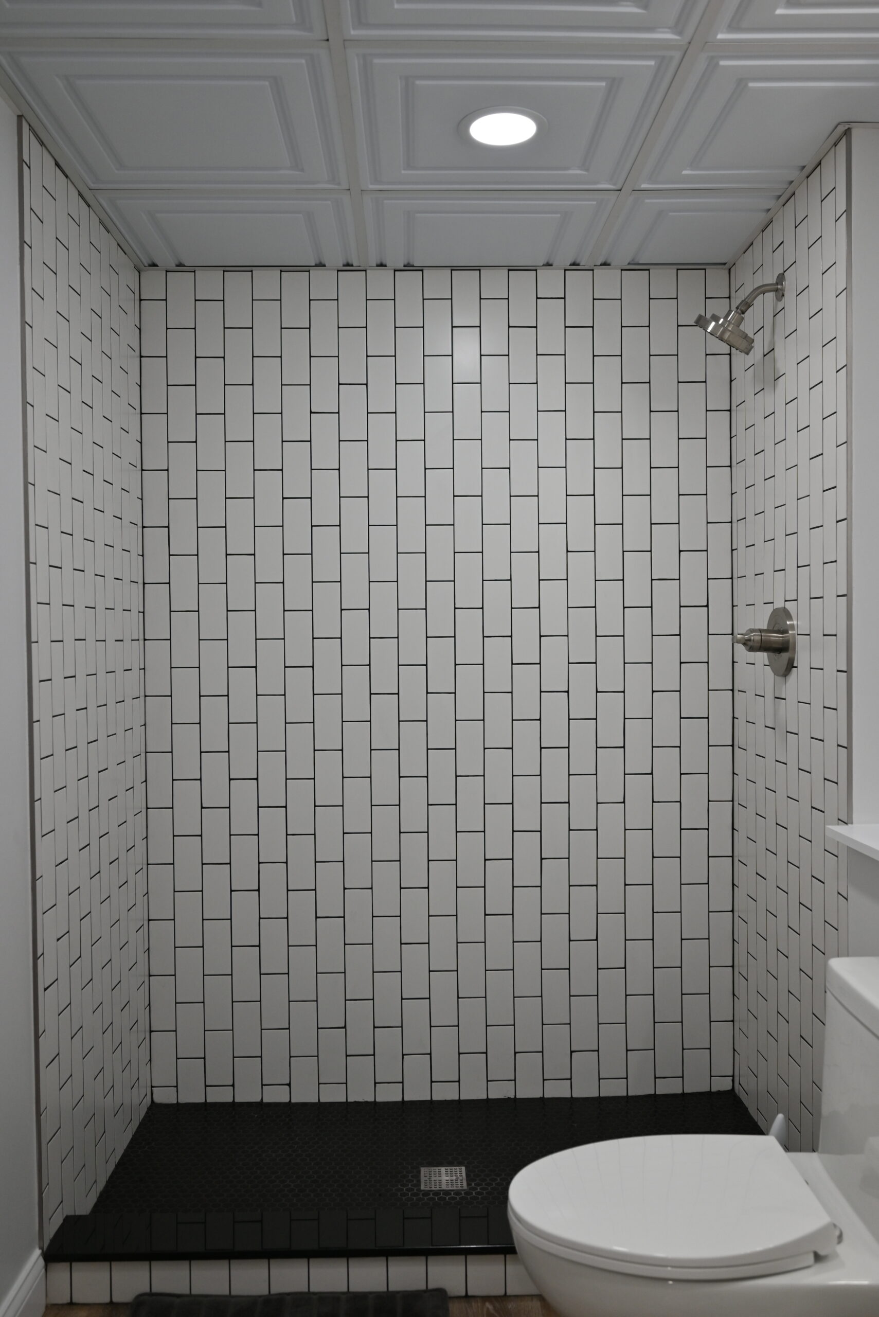 Close-up of custom tiled shower with white basketweave subway tile on walls, black penny round floor tile, and brushed nickel fixtures