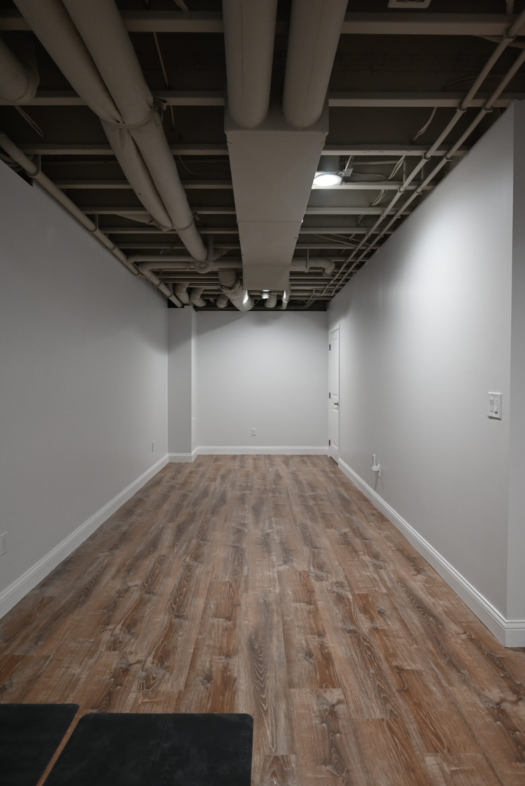 Empty finished basement room with luxury vinyl plank flooring, painted walls, exposed black ceiling, and recessed lighting
