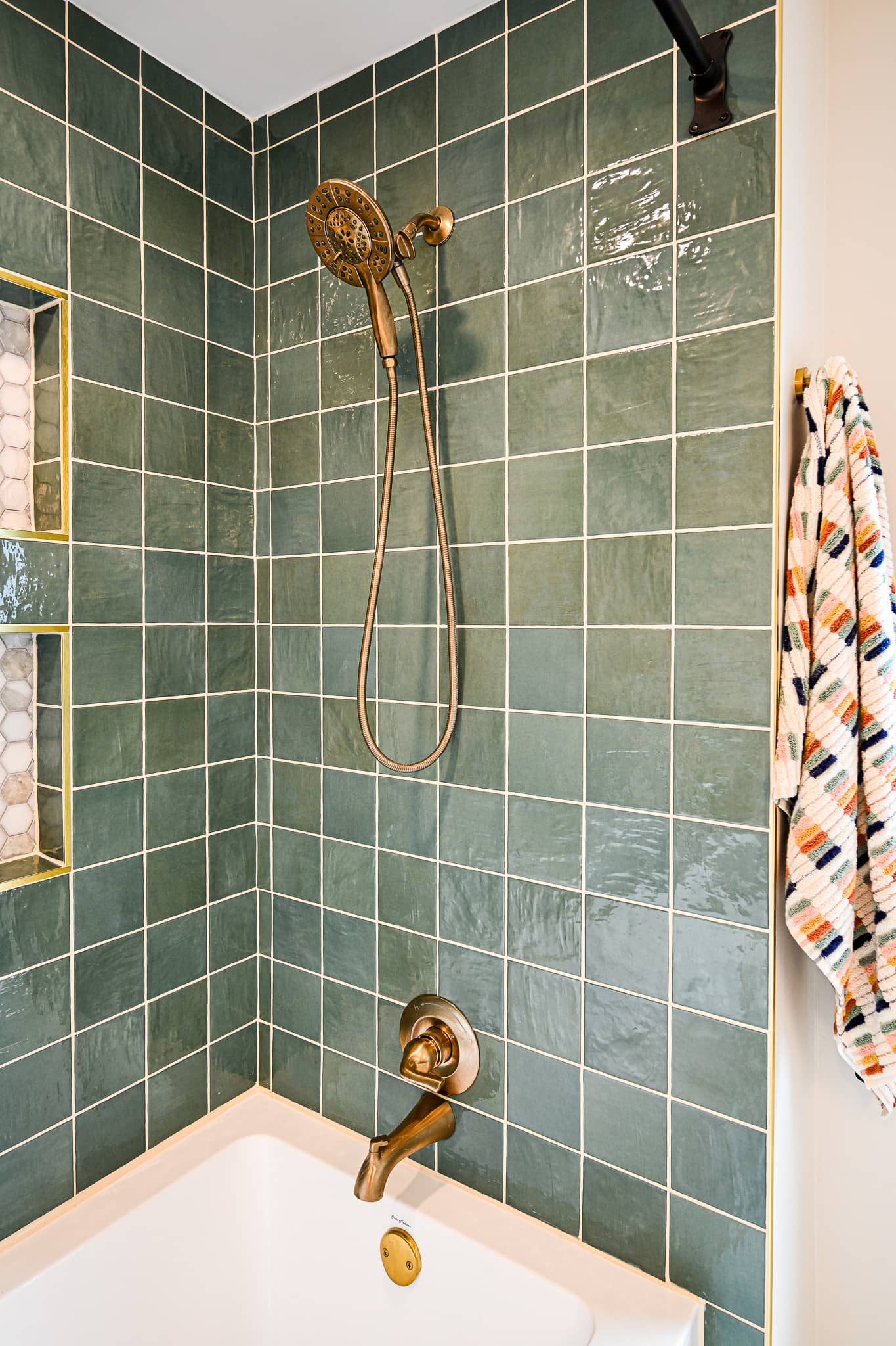 Green square tile shower surround in the Dexter bathroom with an aged brass handheld shower head and tub spout