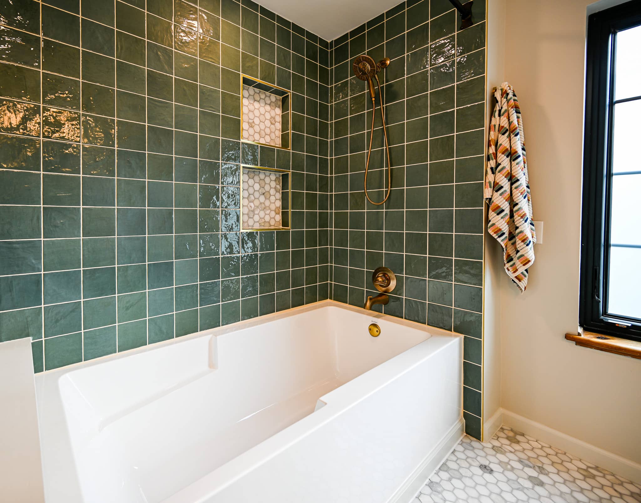 Tub and shower wall with two recessed niches trimmed in brass over a marble hexagon back