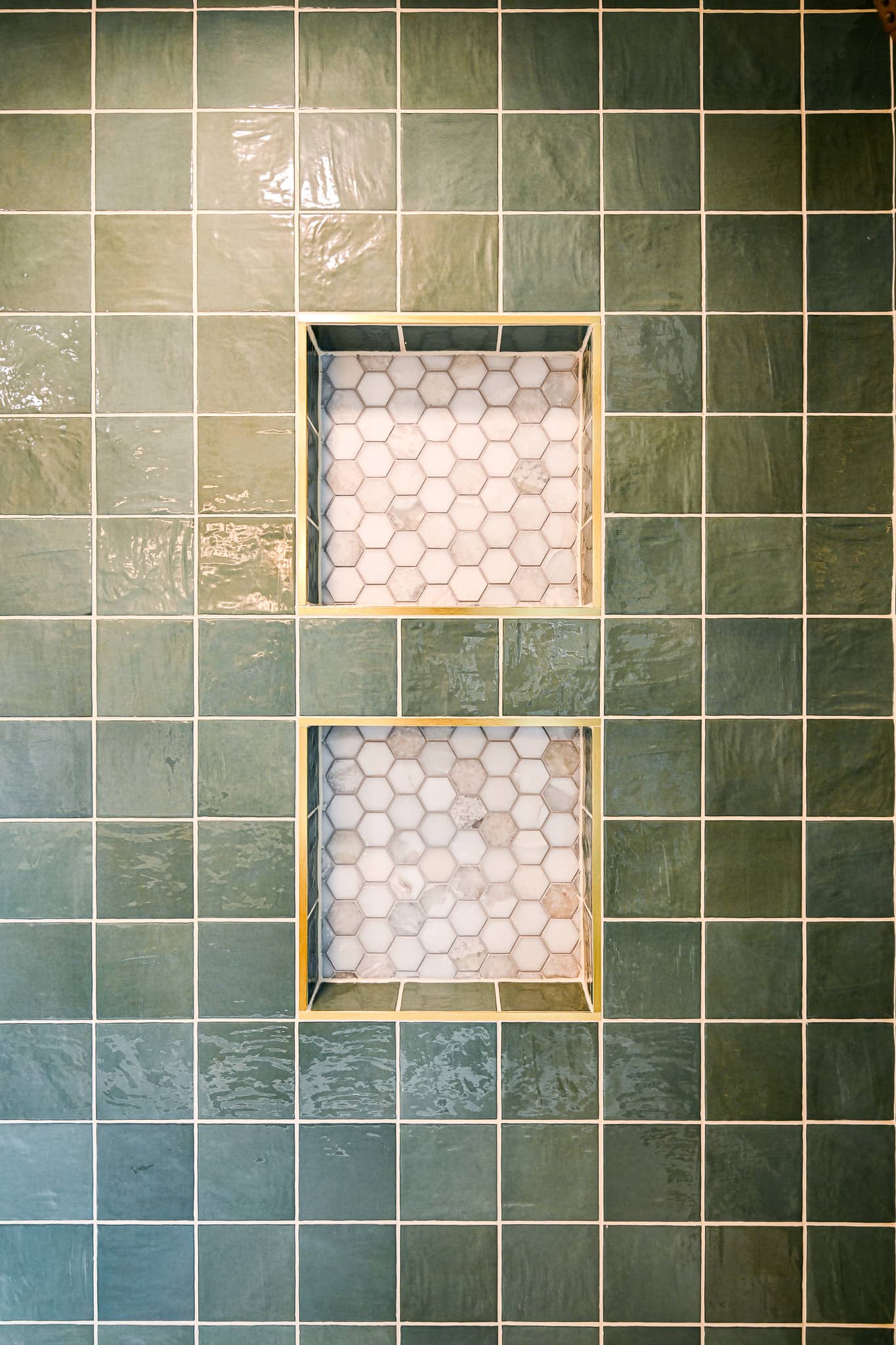 Close view of the recessed shower niches trimmed in brass with a marble hexagon mosaic back