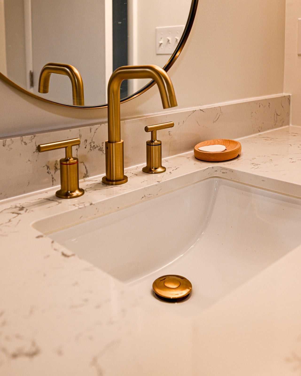 Brushed brass widespread faucet and undermount sink set into a marble-look quartz vanity top