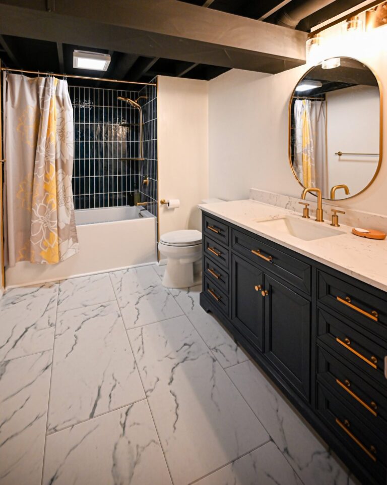 Finished basement bathroom in Ann Arbor with a navy tiled tub surround, a navy vanity with brass fittings and marble-look tile flooring