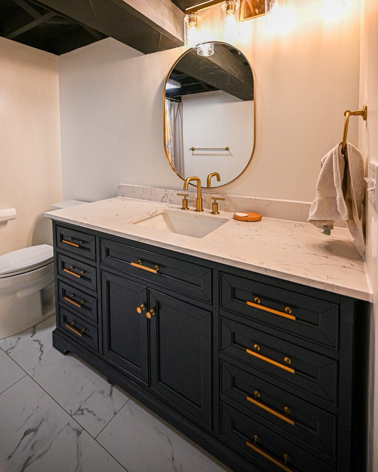 Navy blue bathroom vanity with brass hardware, a quartz top and a brass framed oval mirror in an Ann Arbor basement