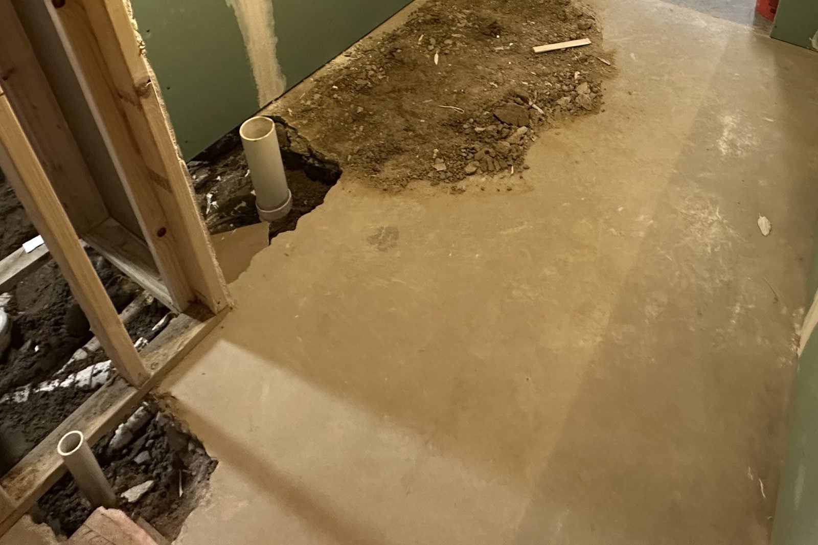 Basement bathroom rough-in with the concrete slab cut open and white PVC drain stubs standing in the trench