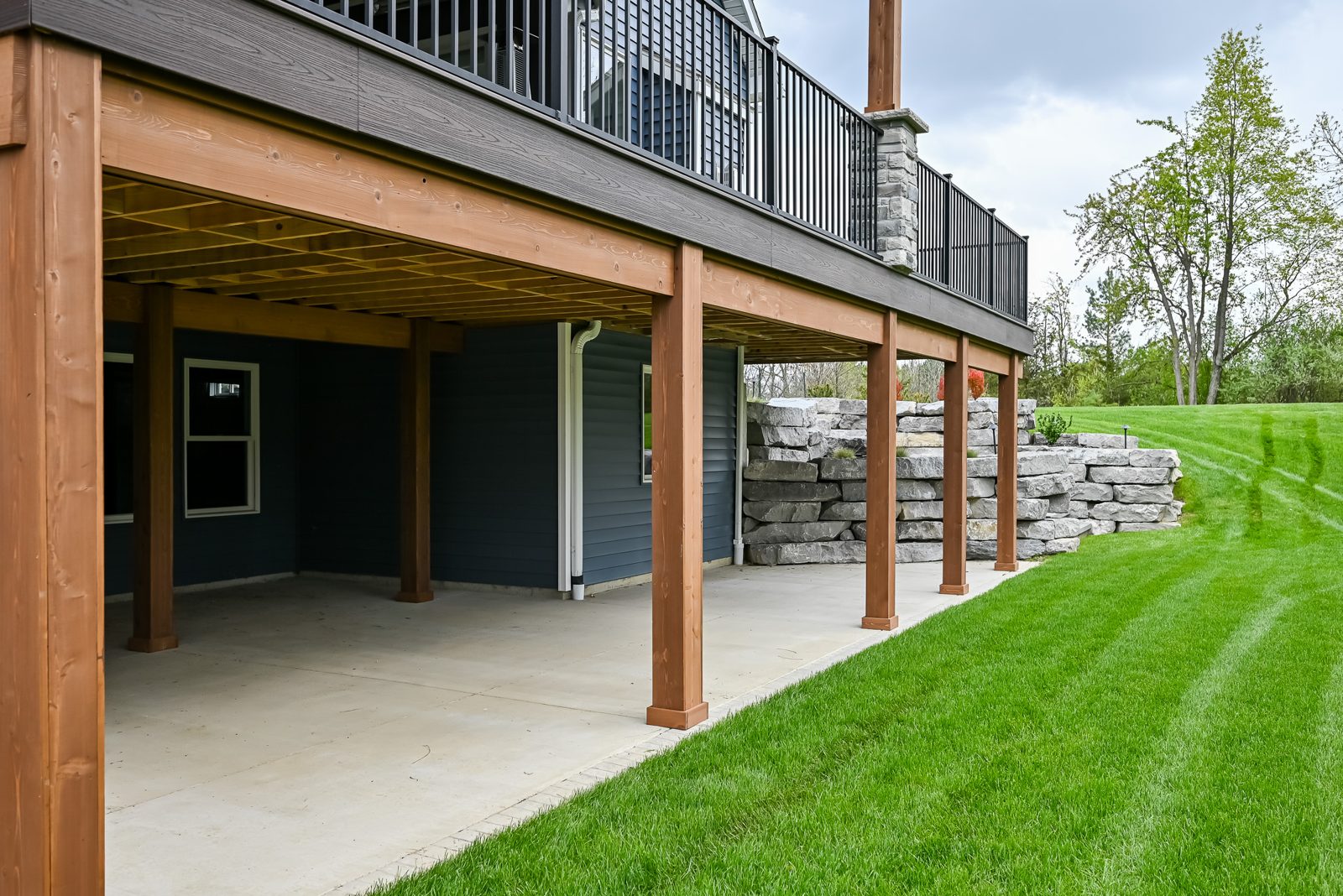 Row of cedar-wrapped deck posts along the lawn and stone wall of an Ann Arbor backyard