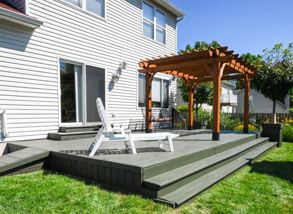 Refinished gray wood deck with wide steps, a white lounge chair and a cedar pergola