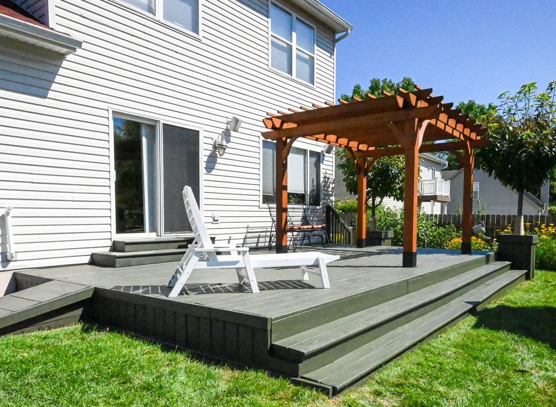 Refinished wood deck in Ann Arbor with wide stained steps, a rebuilt ramp along the house and a cedar pergola