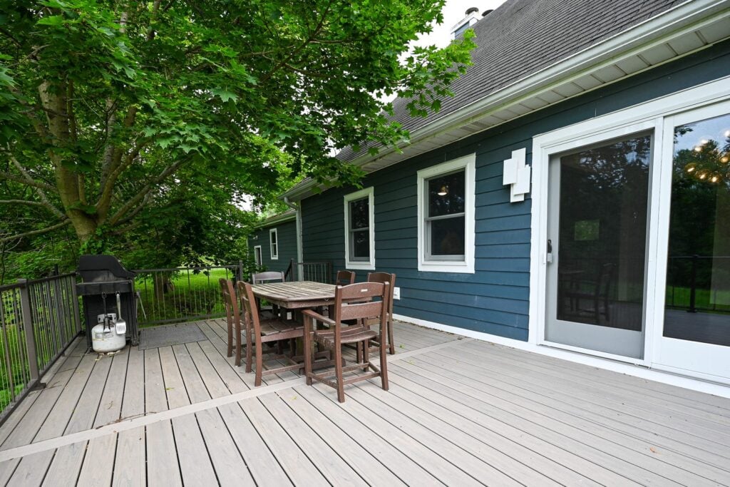 Composite deck with a wood dining table outside a patio door and blue lap siding