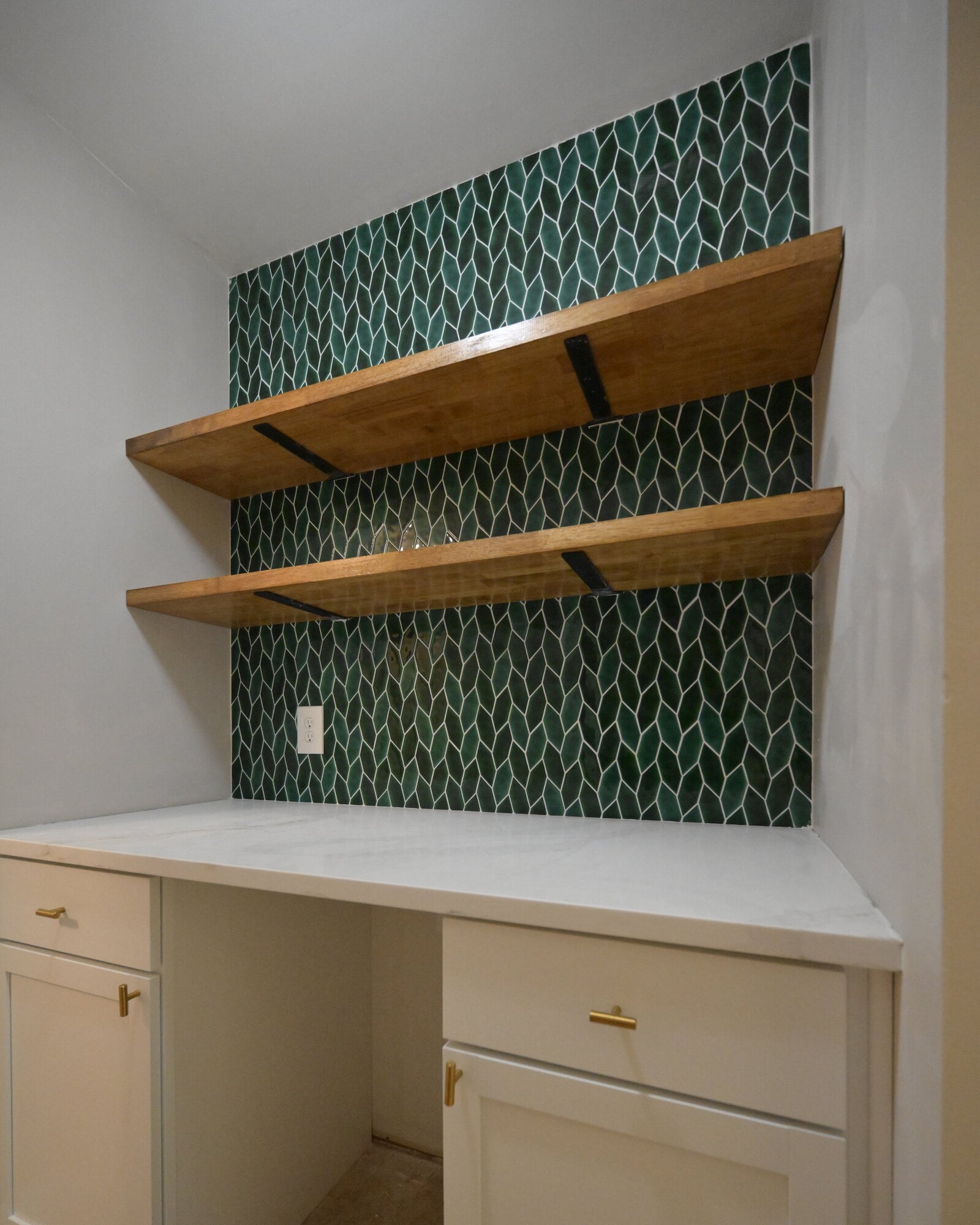 Full elevation of a finished dry bar alcove with cream painted shaker cabinets, brass bar pulls, a white countertop and a green tiled wall
