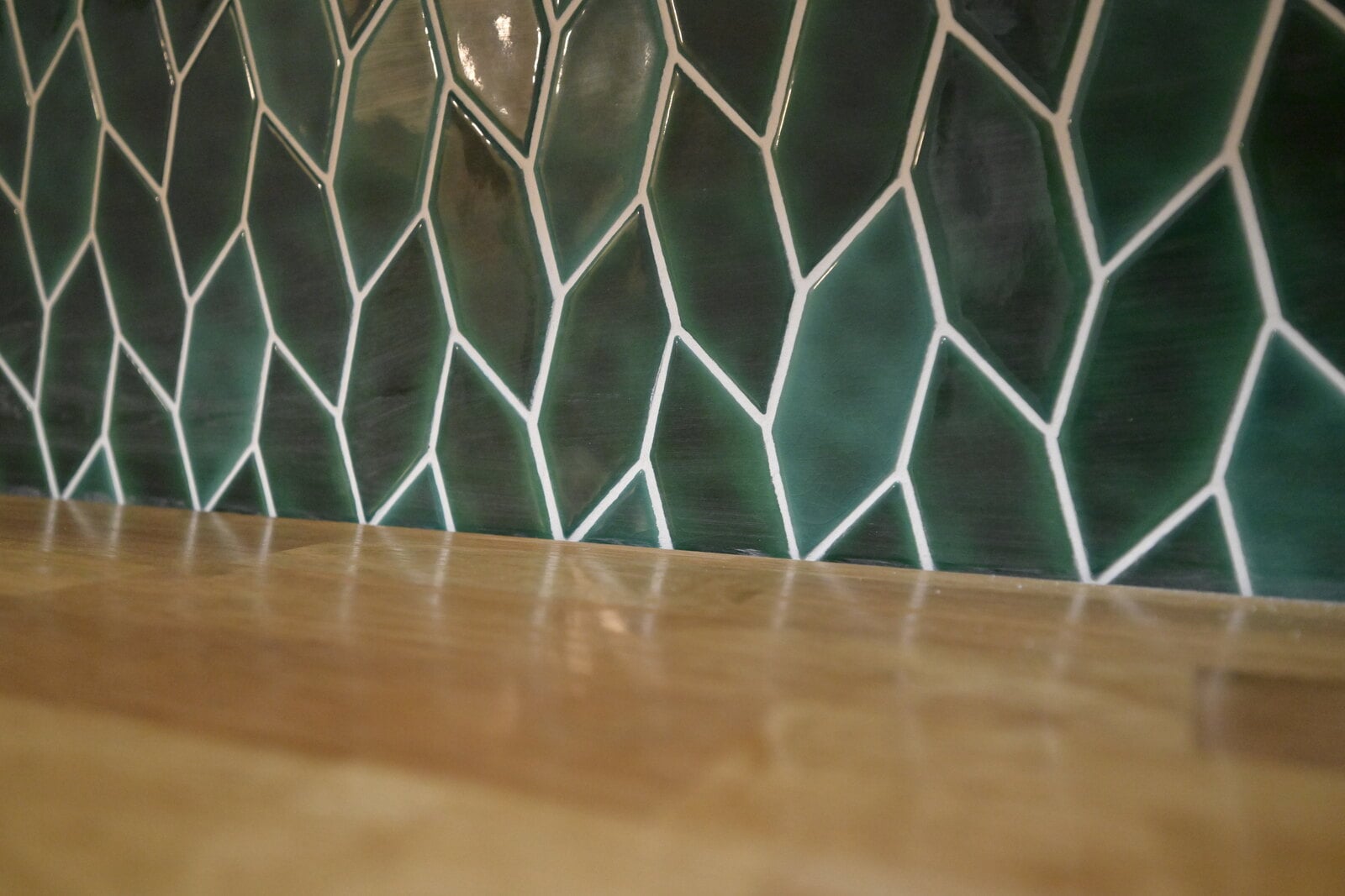 Close view of glossy emerald green leaf-shaped tile with white grout meeting the edge of a stained butcher block shelf