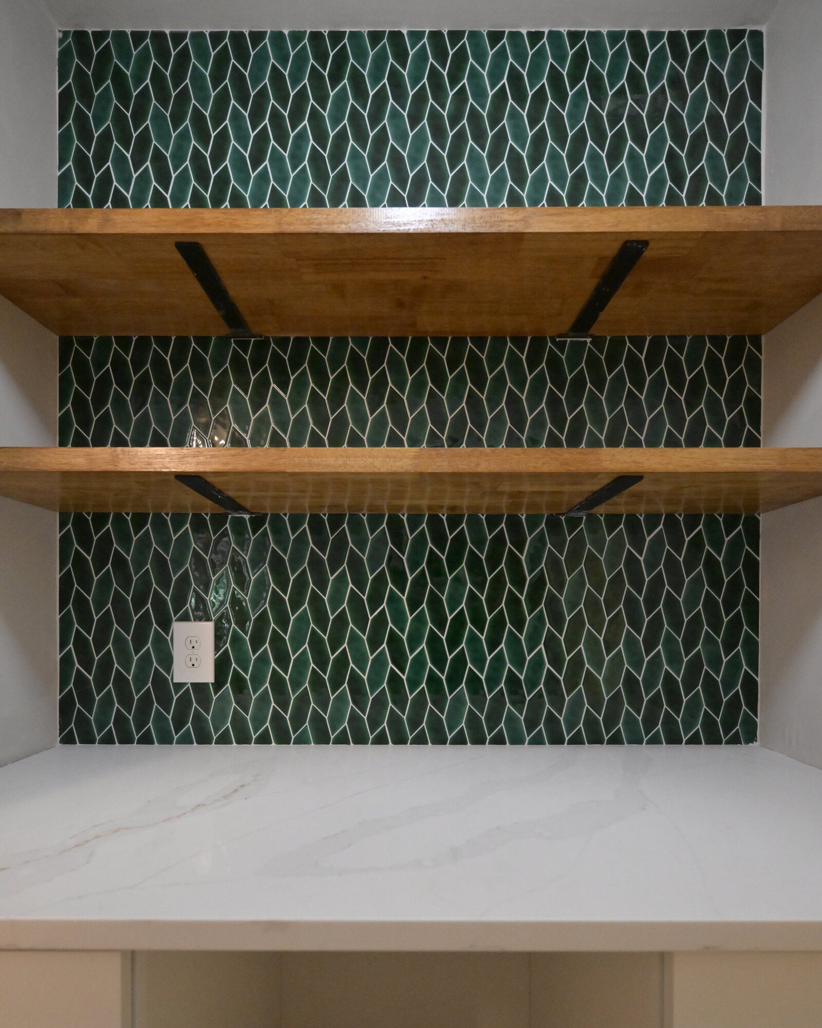 Straight-on view of a finished dry bar showing two butcher block shelves, green tile, a white counter and the open bay left for a mini fridge