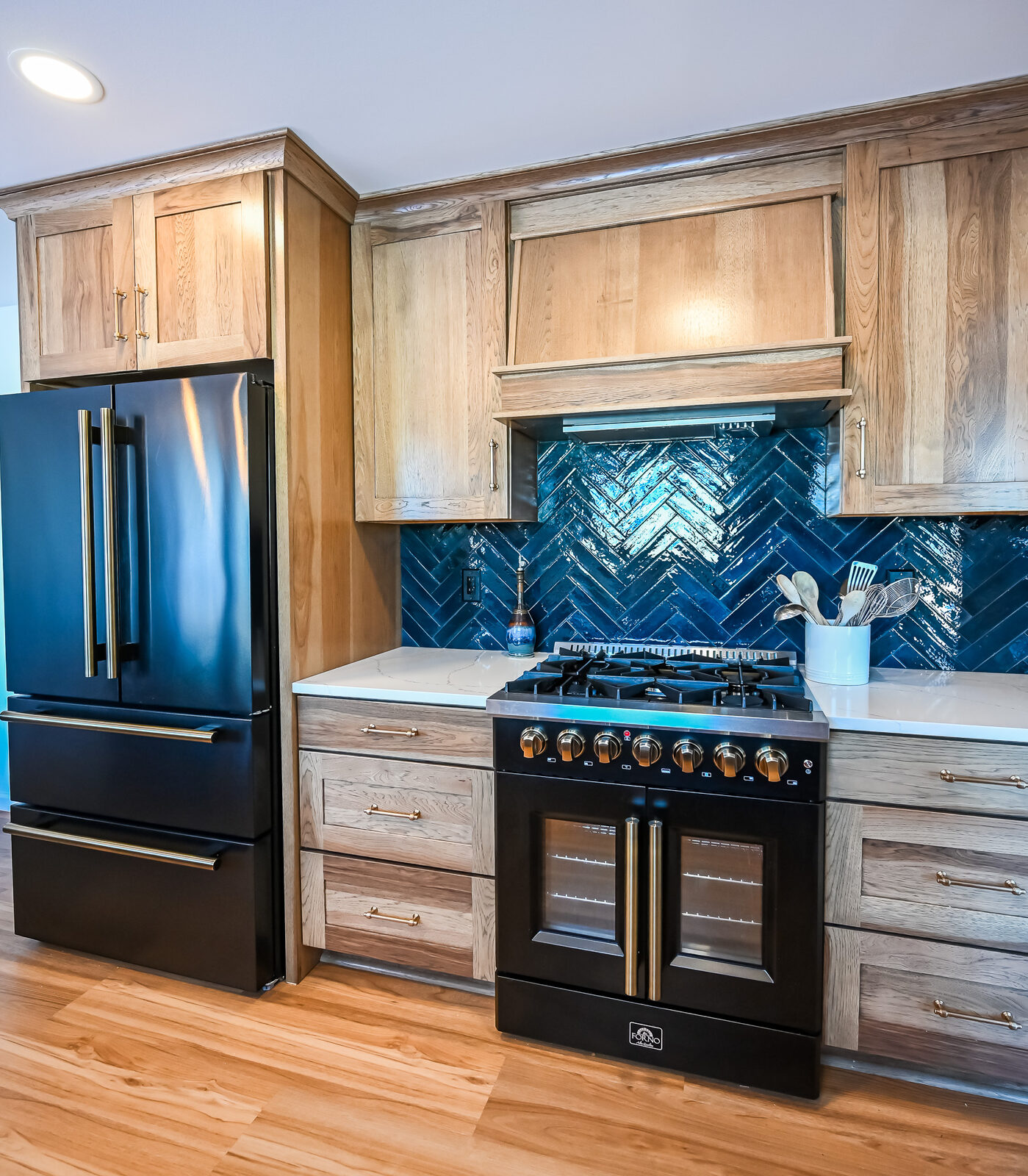 Black French-door refrigerator and black range with brass hardware set into wood cabinets and navy tile