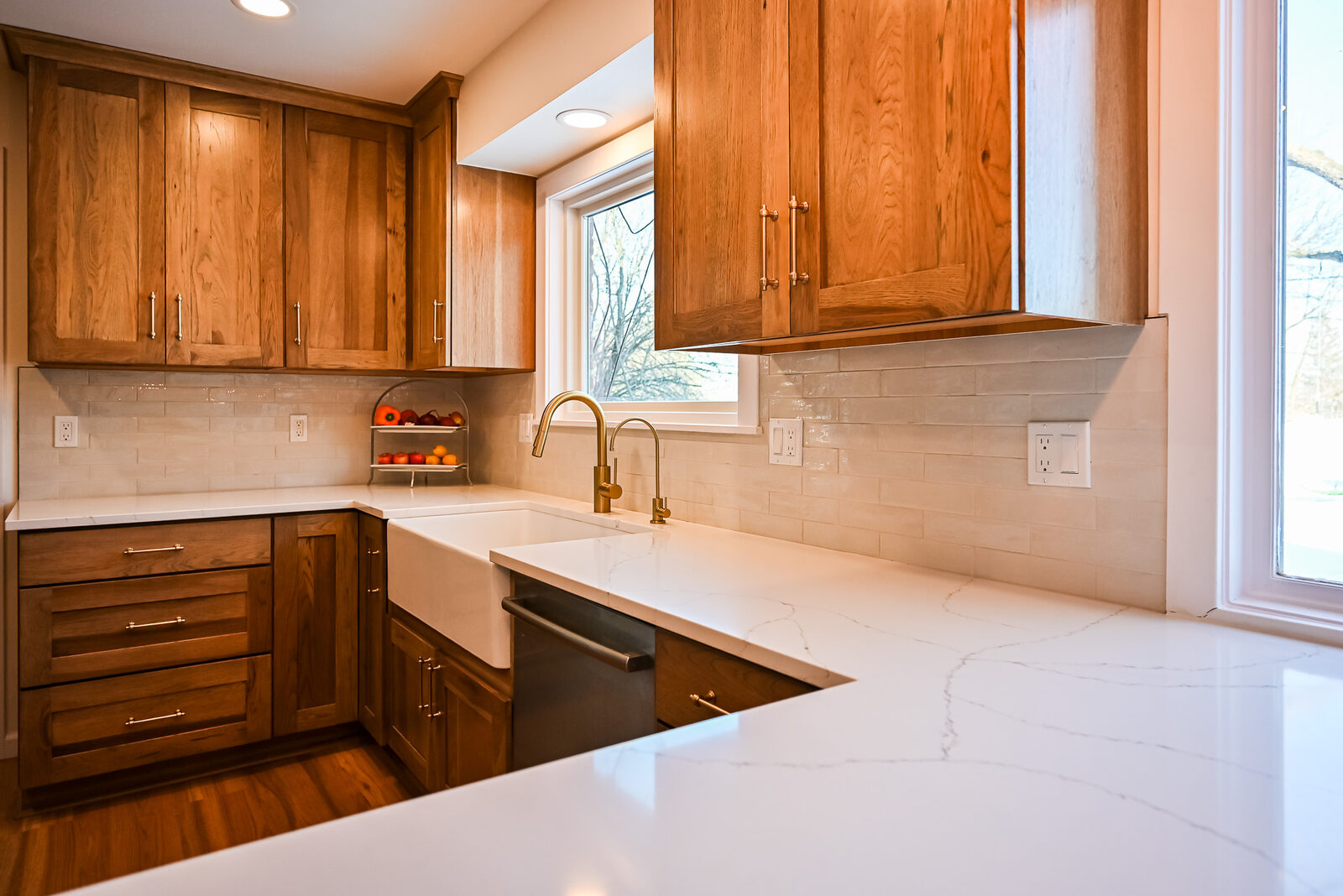 Farmhouse sink with a brass gooseneck faucet against cream tile and white quartz counters in an Ann Arbor kitchen