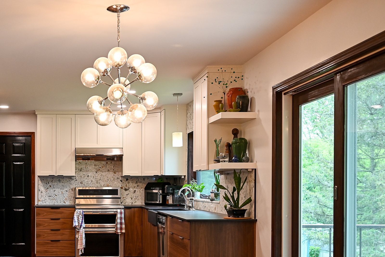 View from the dining room into a remodeled Ann Arbor kitchen with a brass globe chandelier, white upper cabinets and a sliding patio door
