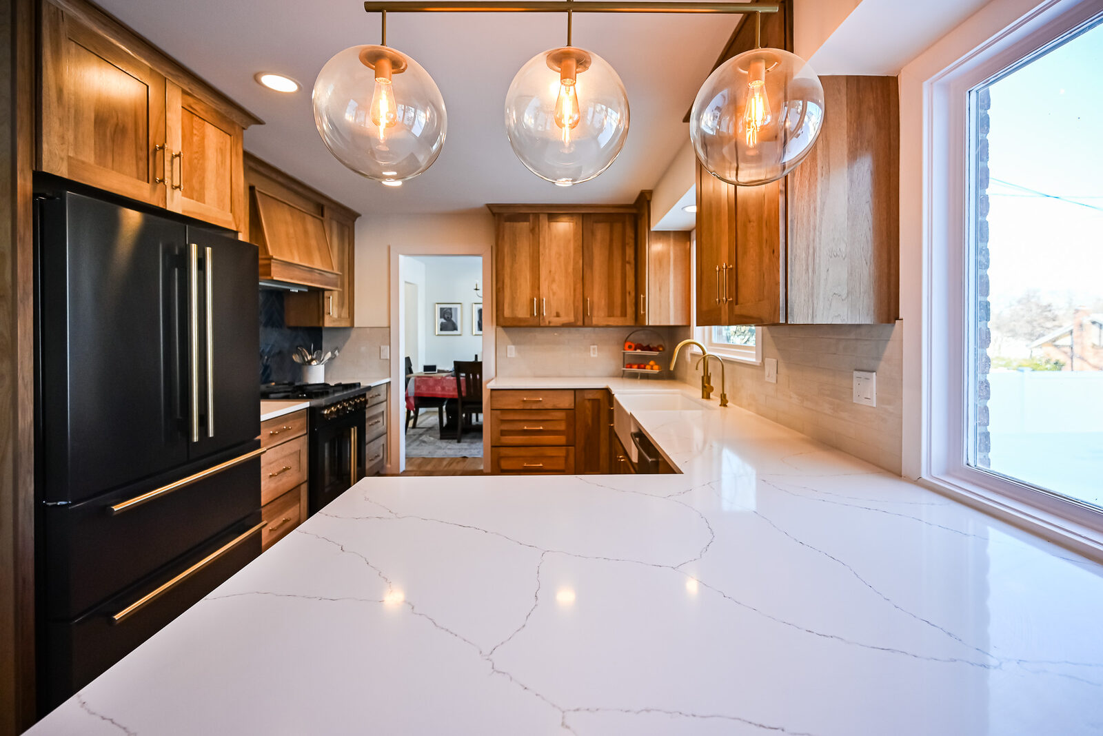 Three clear glass globe pendants on a brass rail above a white quartz counter run in a remodeled kitchen