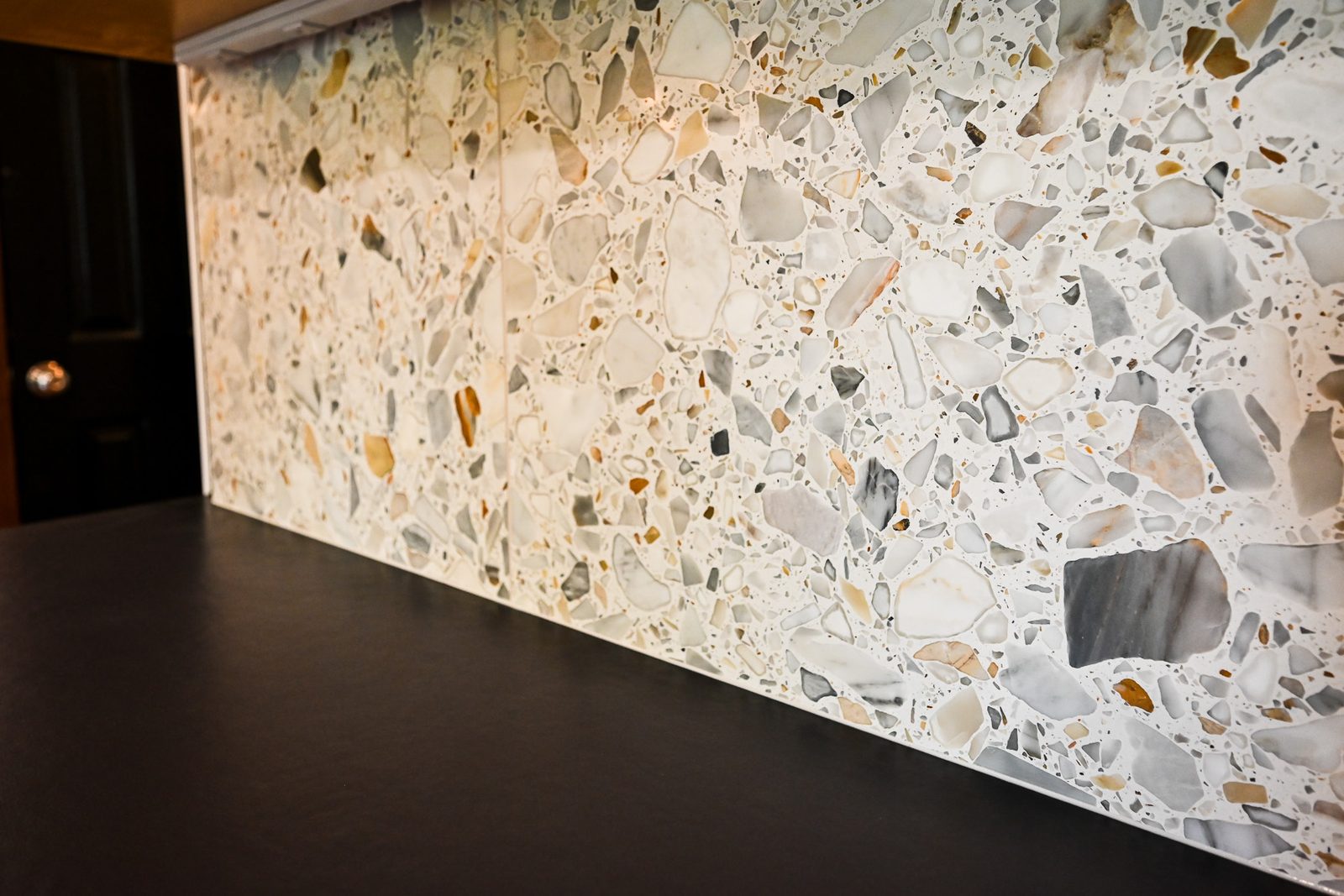Close view of a terrazzo backsplash slab showing large angular white, amber and gray aggregate set in a pale matrix