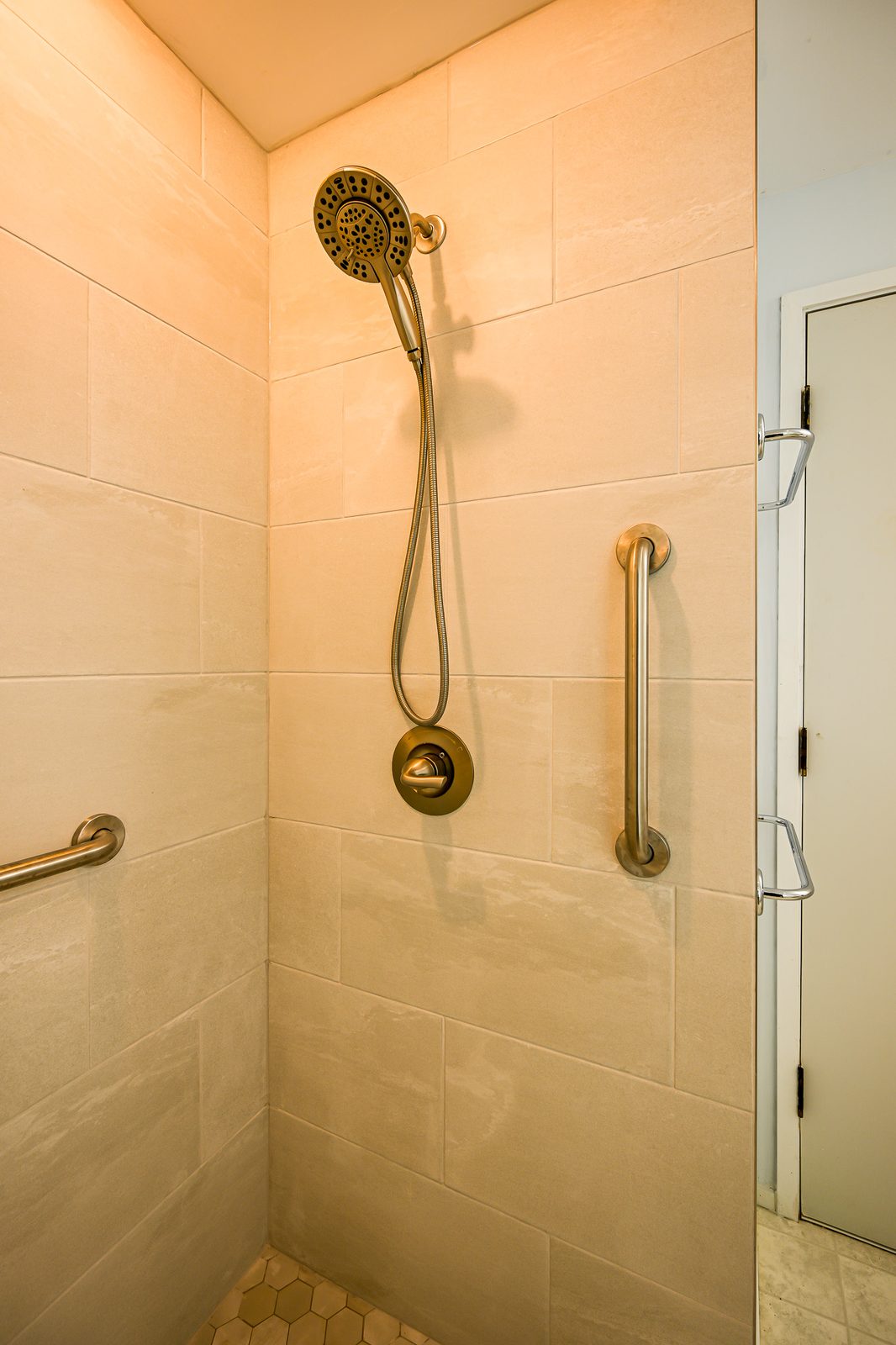 Handheld shower head on a slide bar with grab bars against large-format tile in Ann Arbor