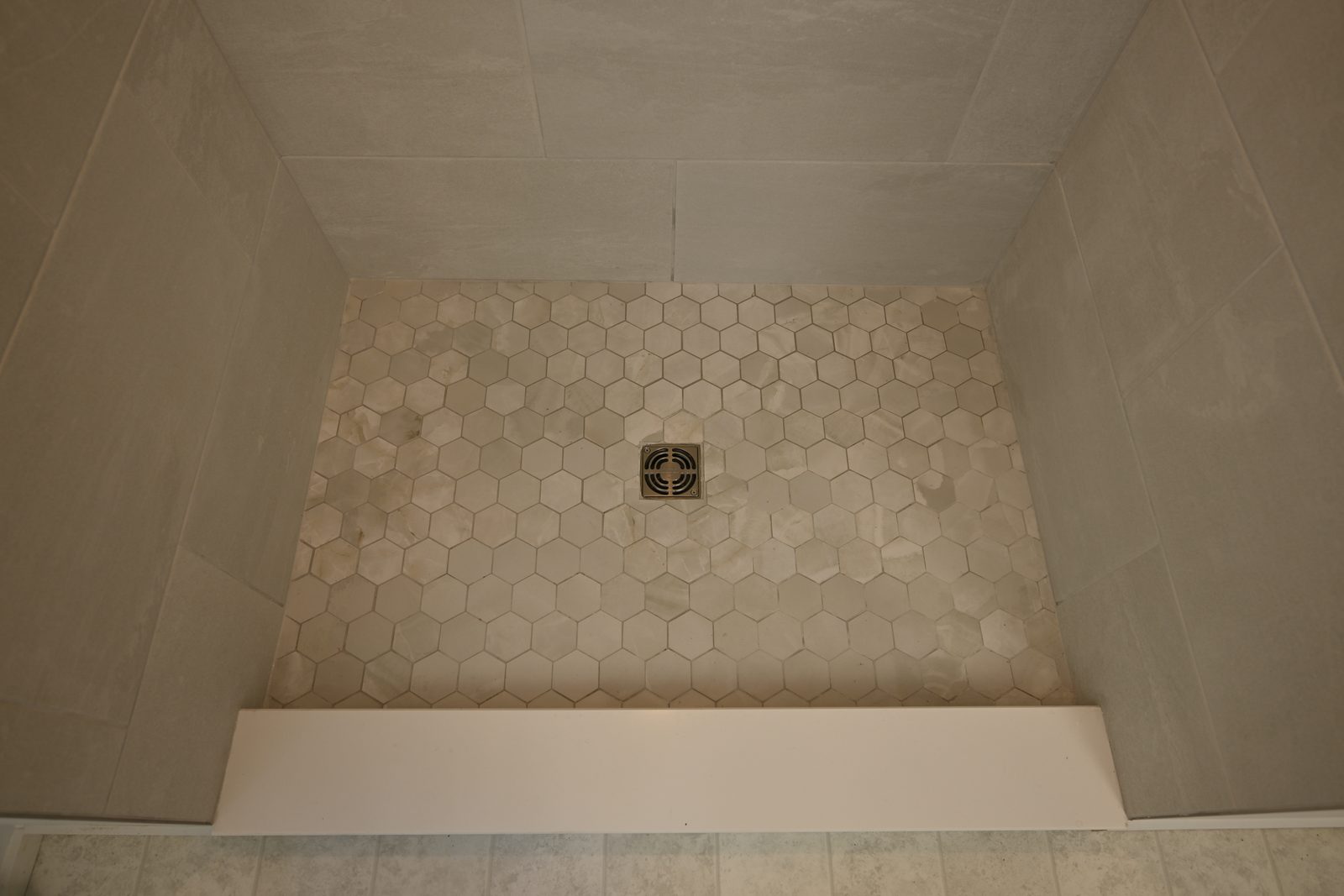 Hexagon mosaic shower floor sloped to a center drain behind a low curb in Ann Arbor