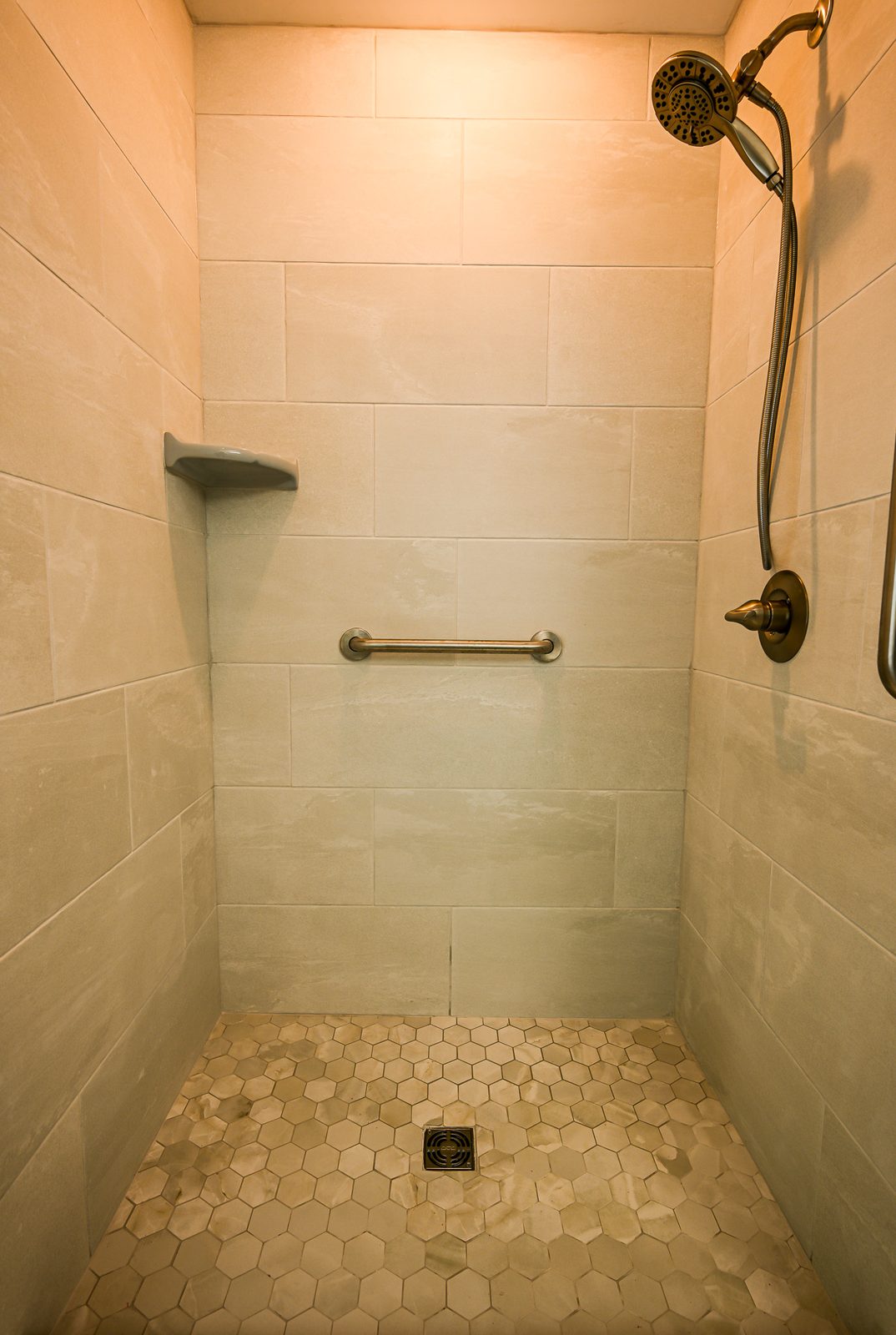 Walk-in shower interior with large-format tile walls, a corner shelf and a hexagon tile floor