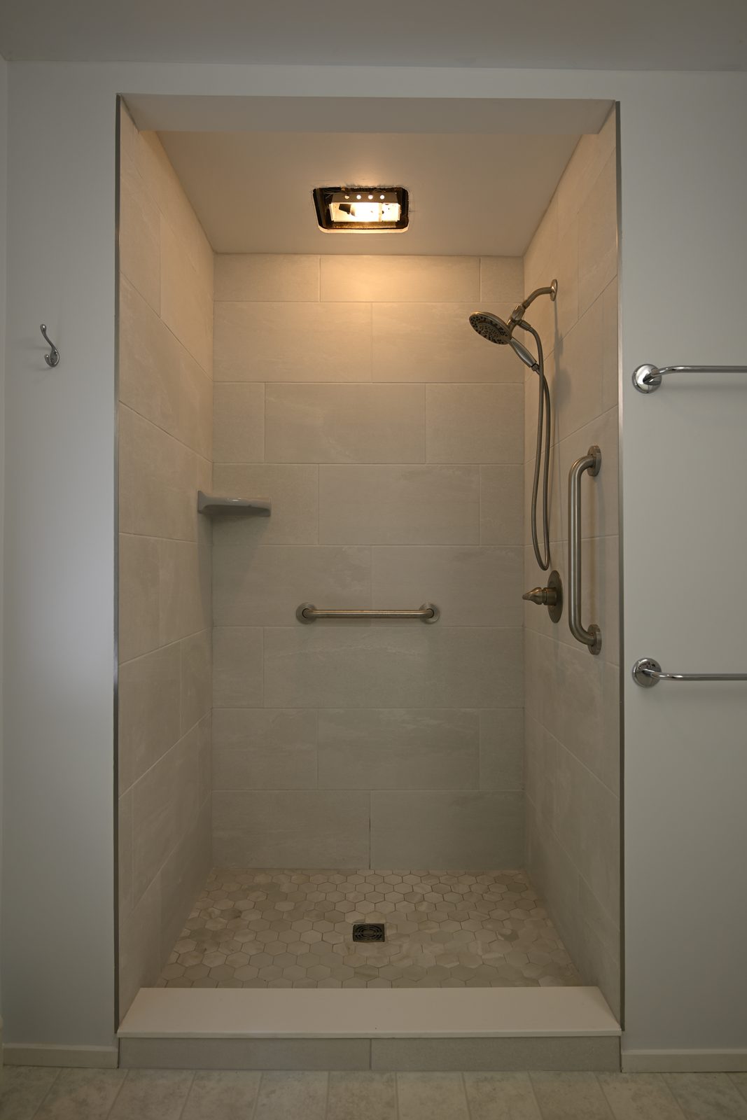 Tiled walk-in shower in the downstairs bathroom of an Ann Arbor home with grab bars and a hexagon mosaic floor