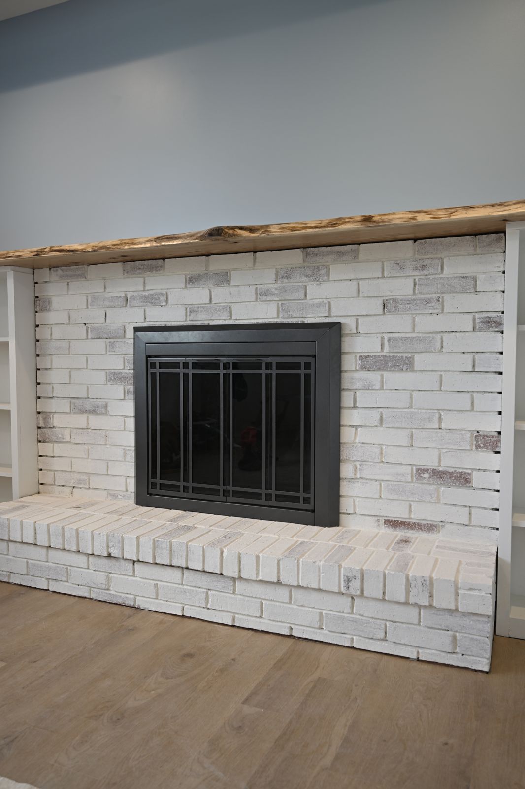 White brick fireplace with a live-edge mantel and built-in shelving in Canton