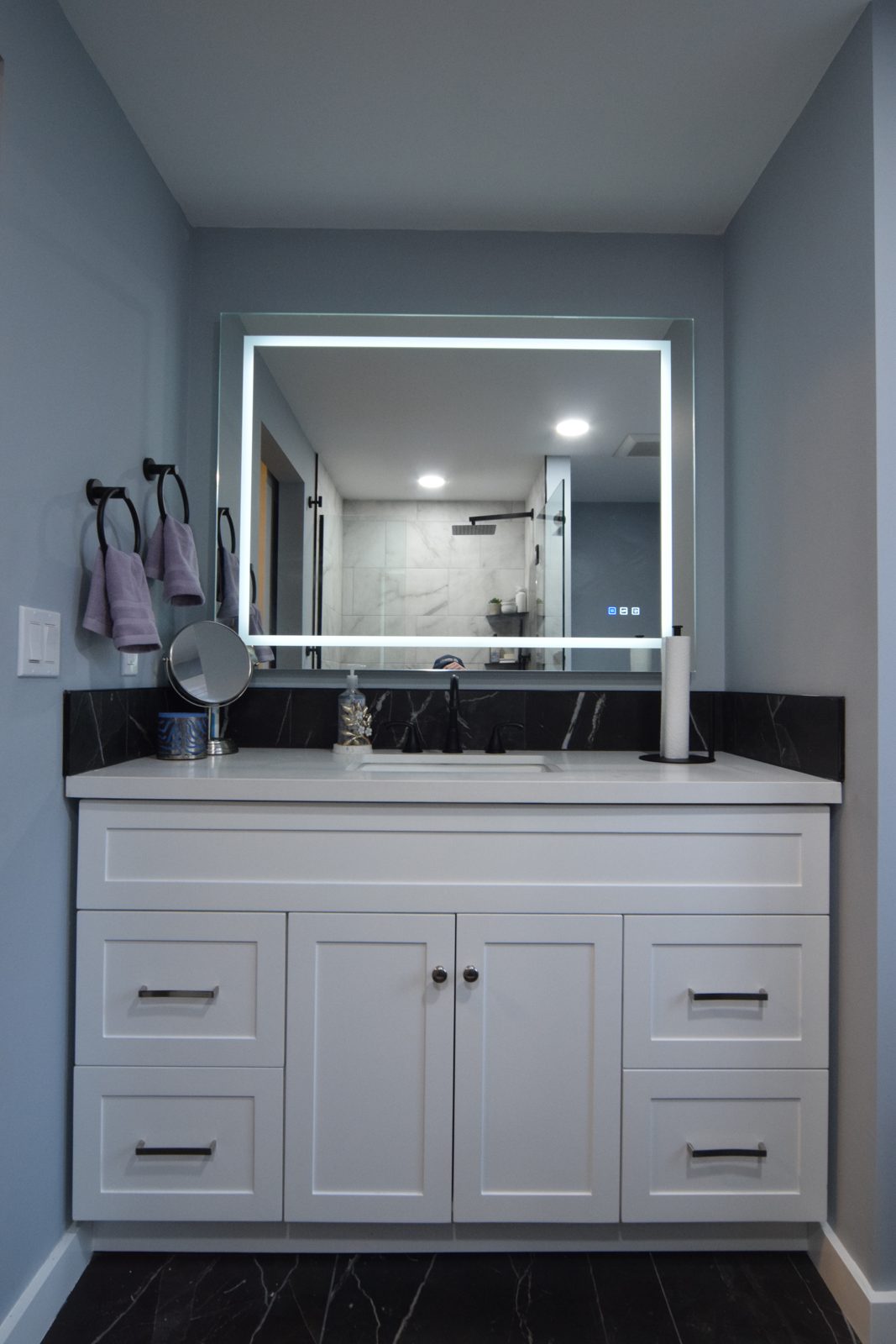 Finished Livonia bathroom vanity with a backlit mirror and a black accent tile wall