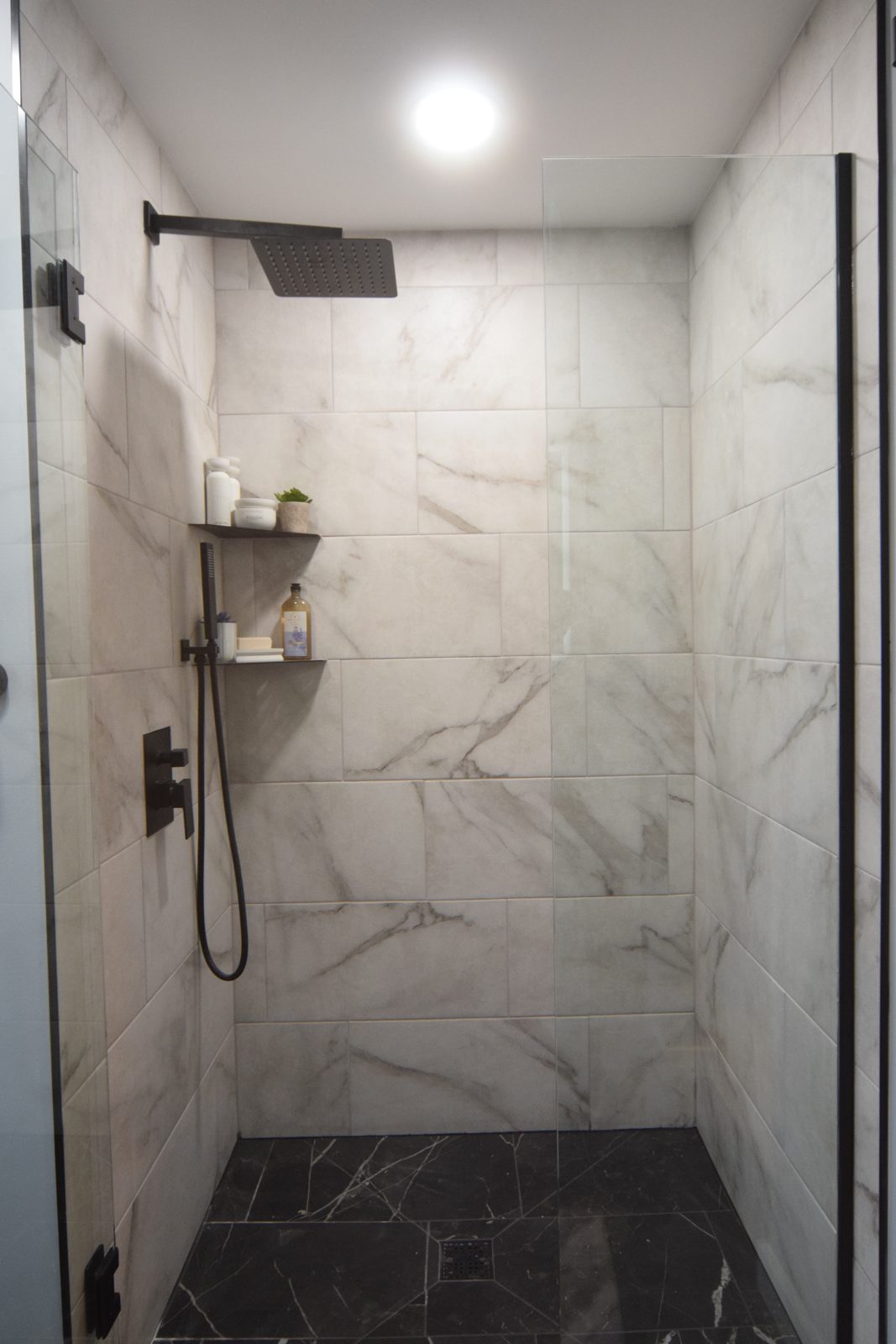 Marble-look large-format tile and a black handheld shower in a finished Livonia bathroom