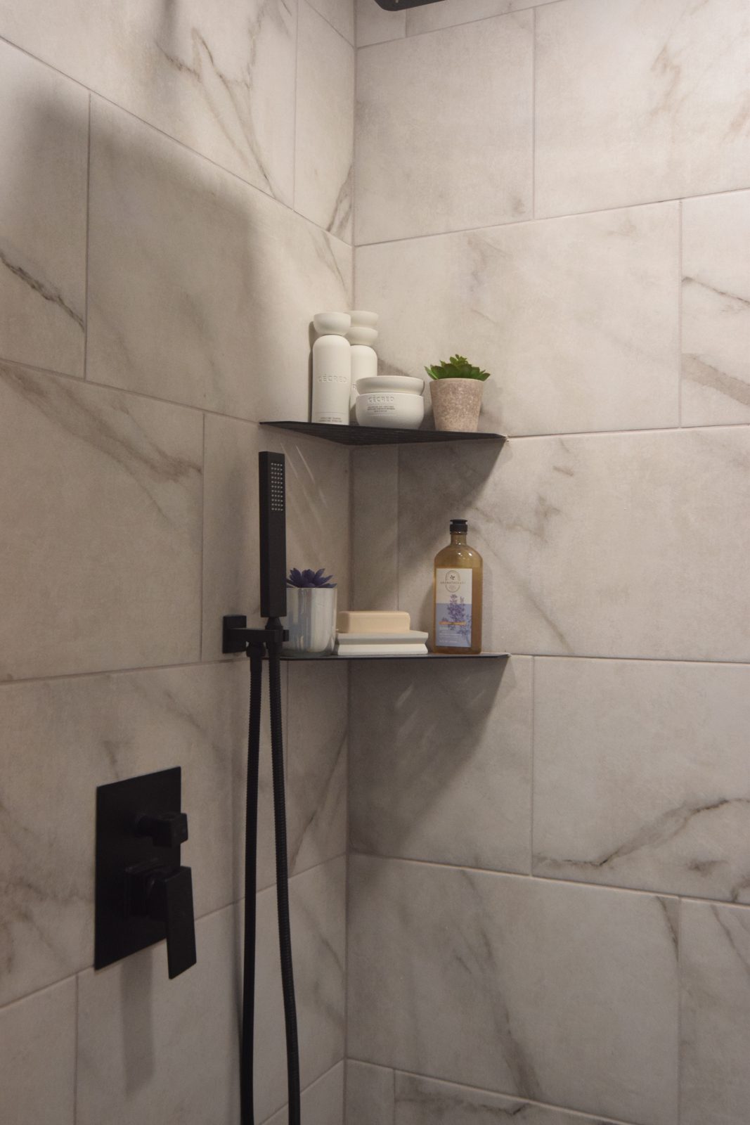 Built-in shower shelf with a matte black bracket against marble-look tile in Livonia