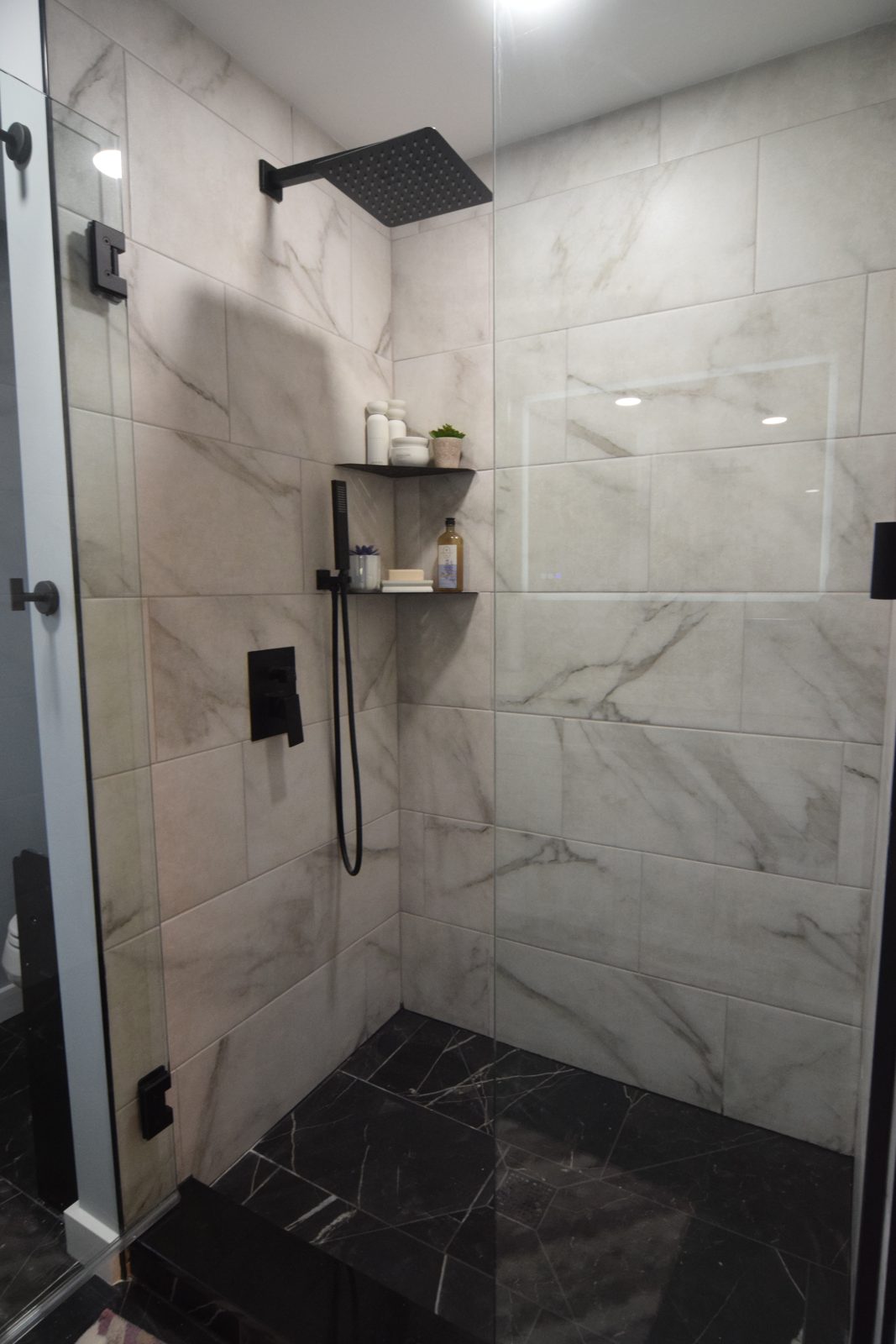 Walk-in glass shower with matte black rainfall fixtures and marble-look tile in Livonia