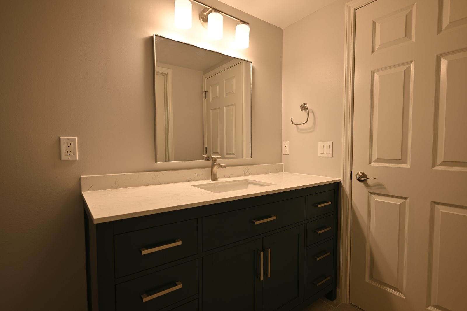 Green vanity with brushed nickel pulls and a white quartz top in a finished Plymouth basement bathroom
