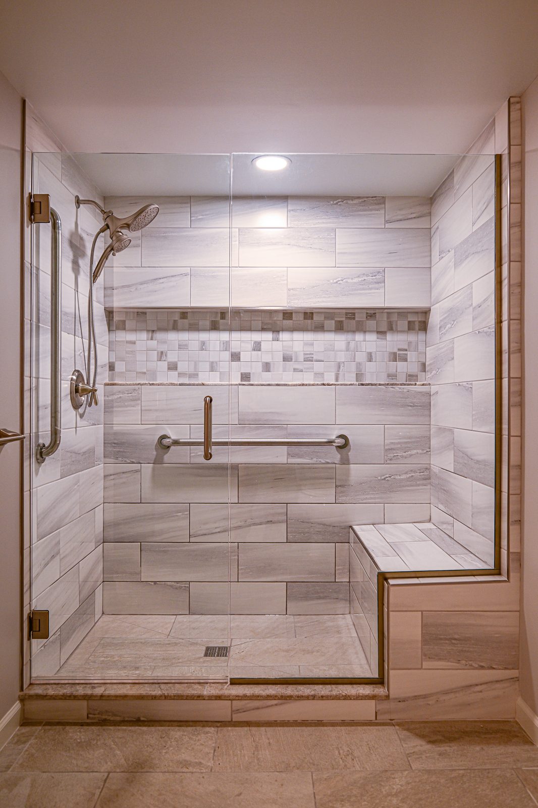 Walk-in shower in Plymouth with a tiled corner bench, mosaic accent band and grab bars