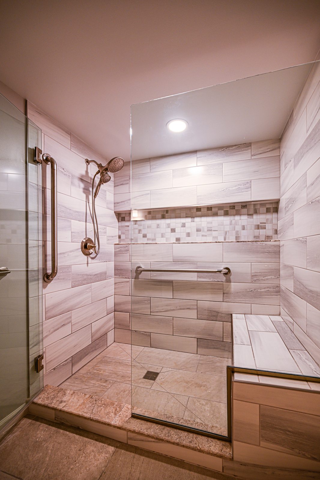 Walk-in shower with a tiled bench, two shower heads and grab bars in a remodeled Plymouth basement bathroom